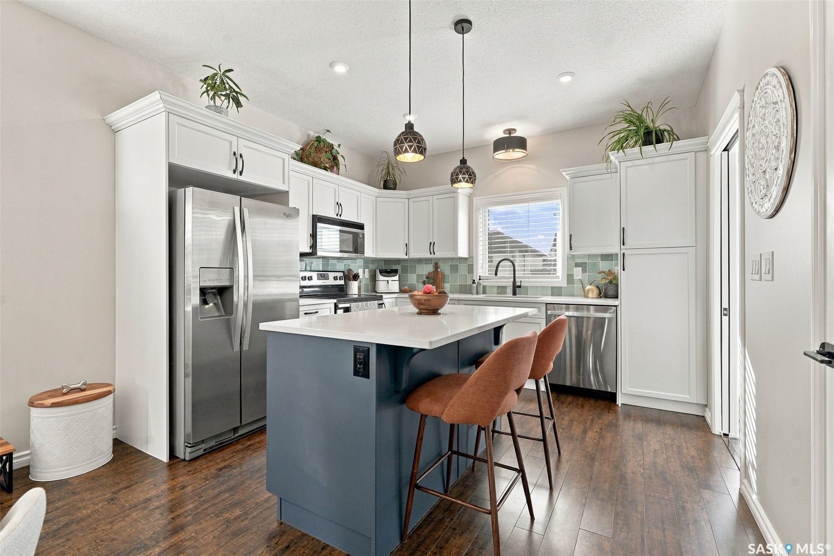 919 Kolynchuk Bend, Saskatoon SK S7T 0V9 Kitchen featuring white upper and lower cabinetry, stainless steel appliances, a center island with a white countertop, wood-finish flooring, and pendant lighting