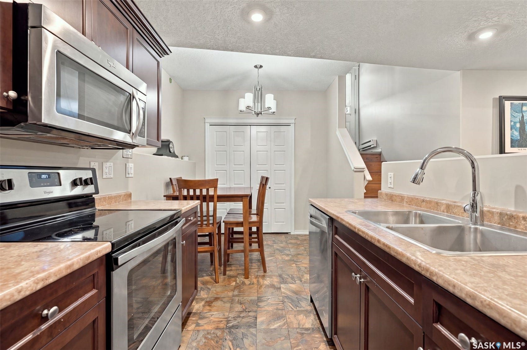 919 Kolynchuk Bend, Saskatoon SK S7T 0V9 Kitchen featuring stainless steel appliances, dark wood-finish cabinetry, light-toned countertops, a double basin sink, and tile flooring
