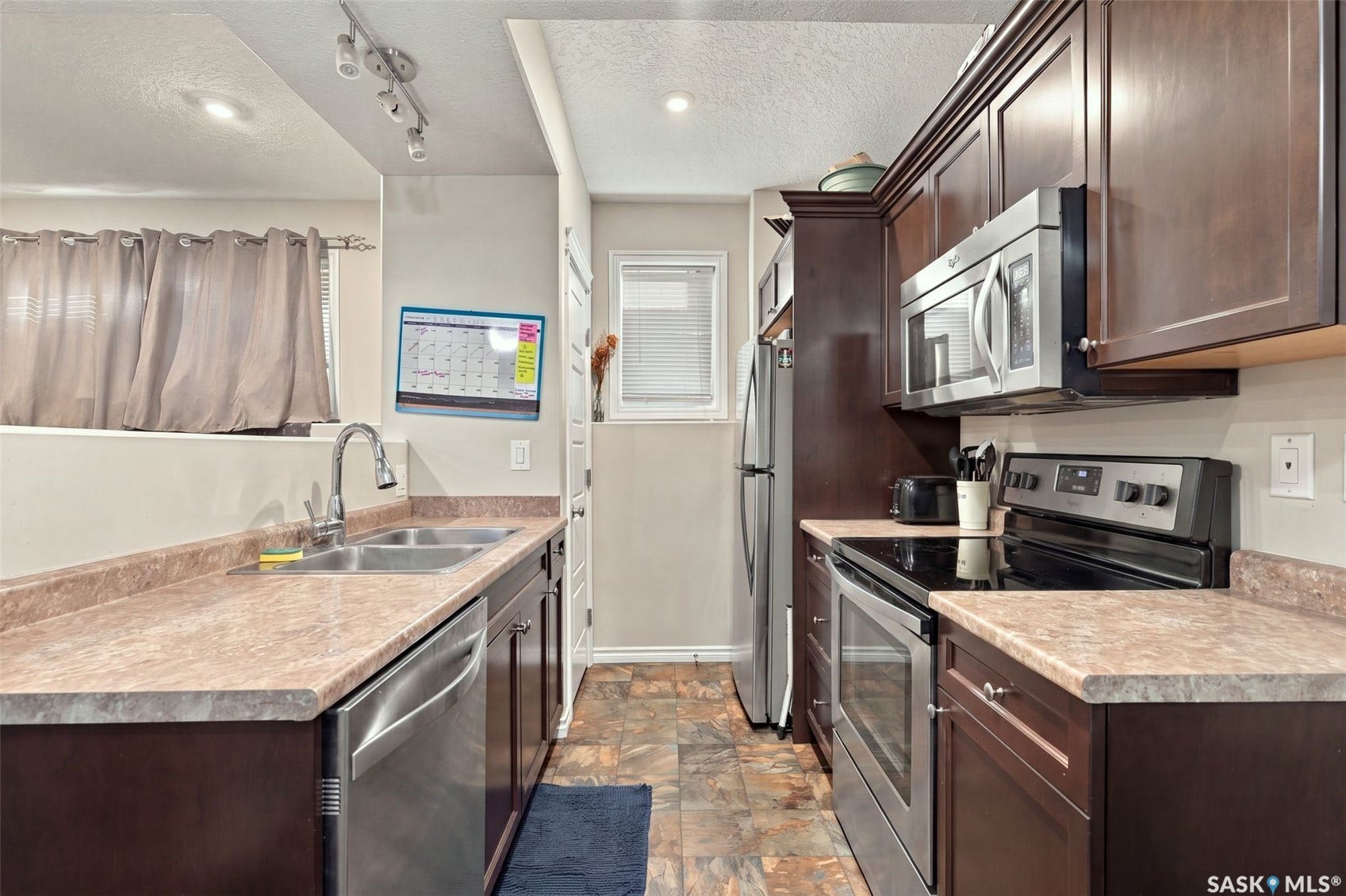 919 Kolynchuk Bend, Saskatoon SK S7T 0V9 Galley kitchen featuring wood-finish cabinetry, stainless steel appliances, a double basin sink, and a built-in microwave