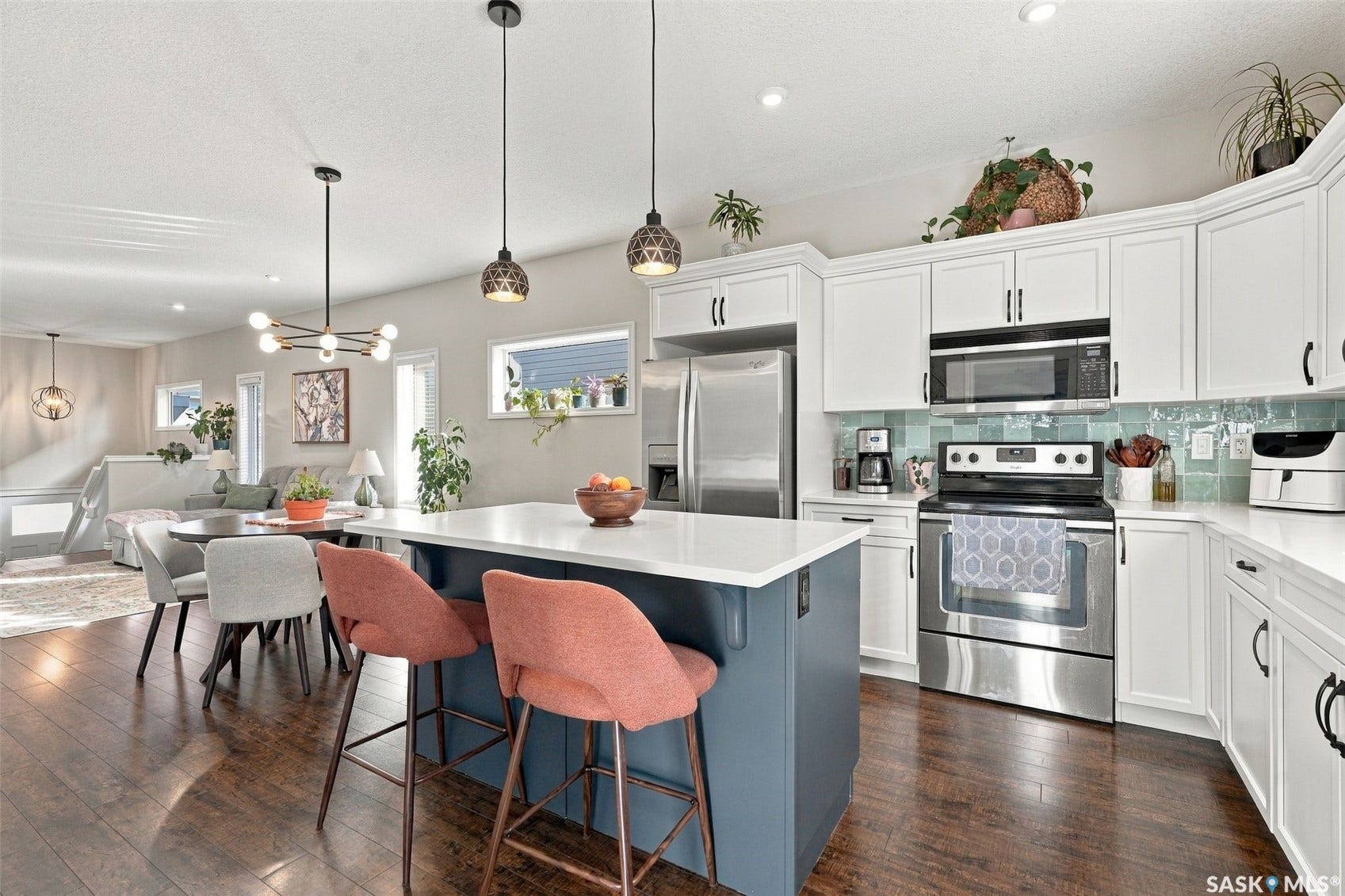919 Kolynchuk Bend, Saskatoon SK S7T 0V9 Open-concept kitchen featuring white cabinetry, stainless steel appliances, a tile backsplash, and a central island with a white countertop