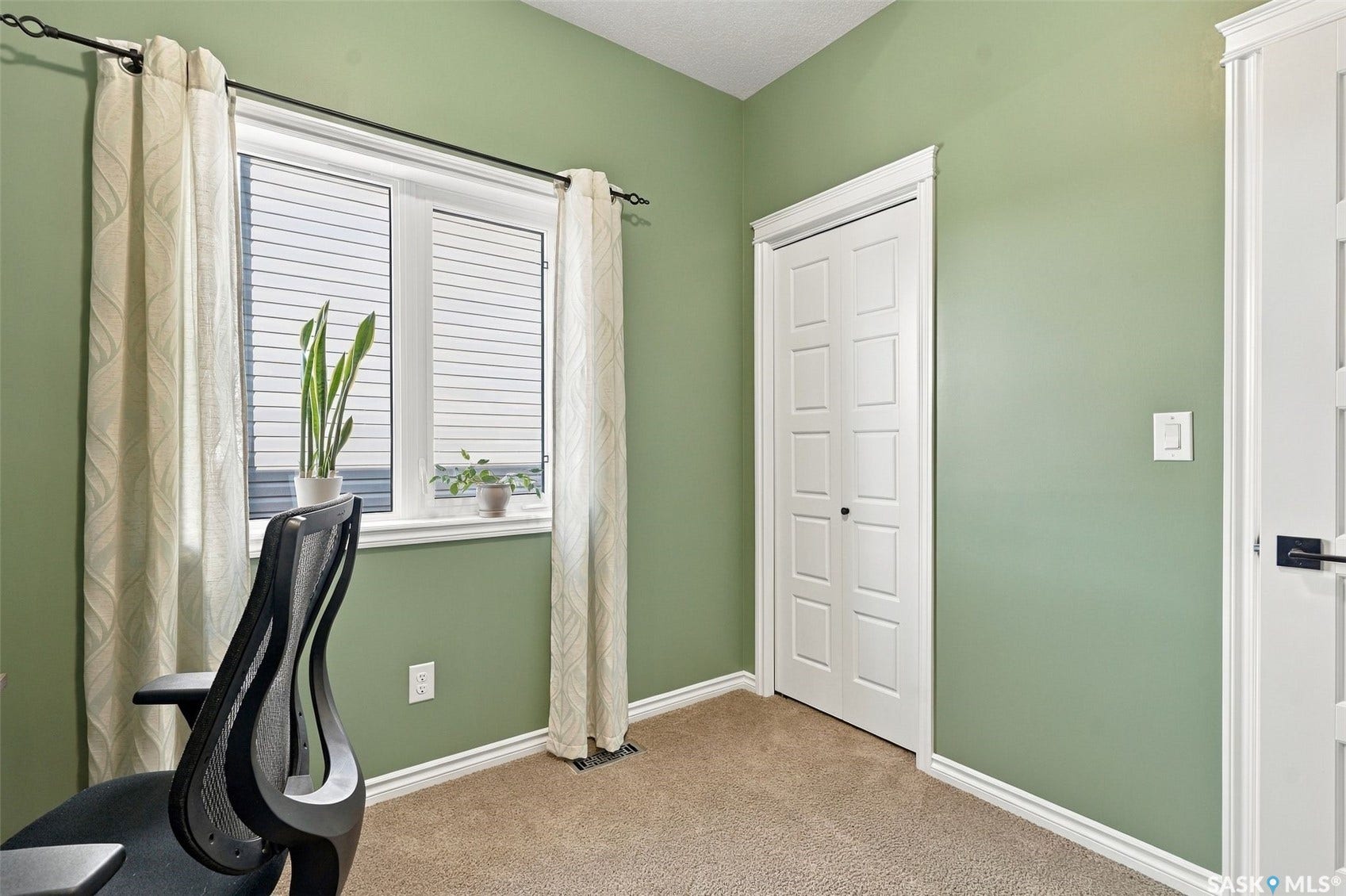919 Kolynchuk Bend, Saskatoon SK S7T 0V9 Window with horizontal blinds and decorative curtains, neutral carpet flooring, light green painted walls, white trim, and a white paneled door