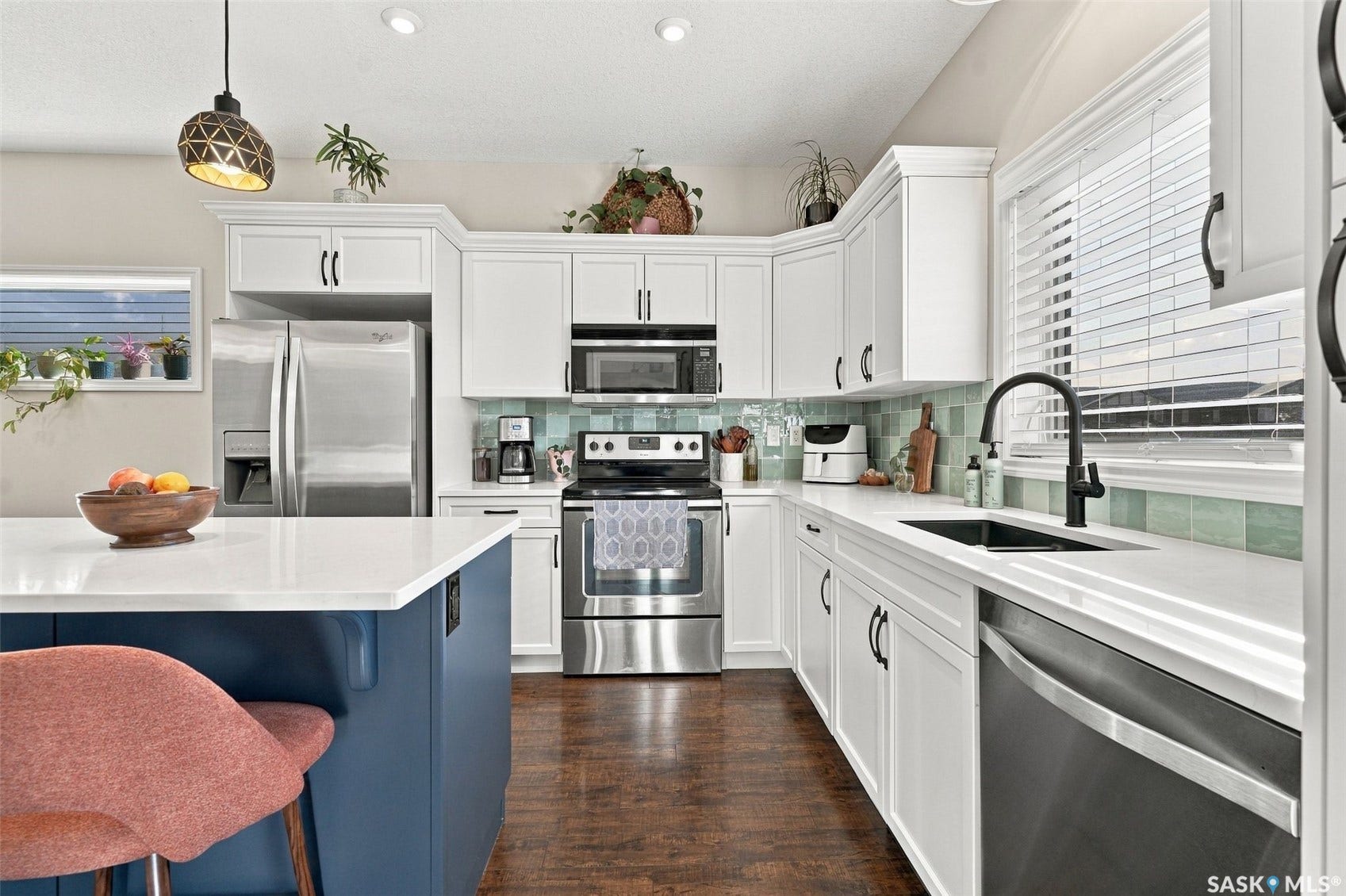 919 Kolynchuk Bend, Saskatoon SK S7T 0V9 White shaker-style cabinetry, stainless steel appliances, a center island with a white countertop, wood-finish flooring, and a tiled backsplash