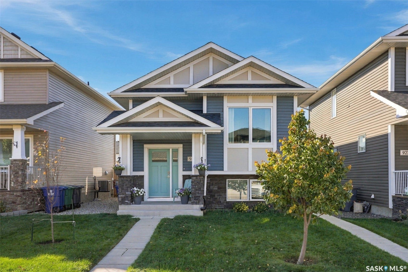 919 Kolynchuk Bend, Saskatoon SK S7T 0V9 Two-story facade with stone accents, covered front entry, light blue door, and front lawn