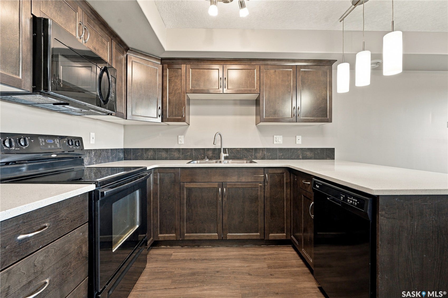 Dark wood-finish cabinetry complemented by white quartz countertops, black appliances, and pendant lighting