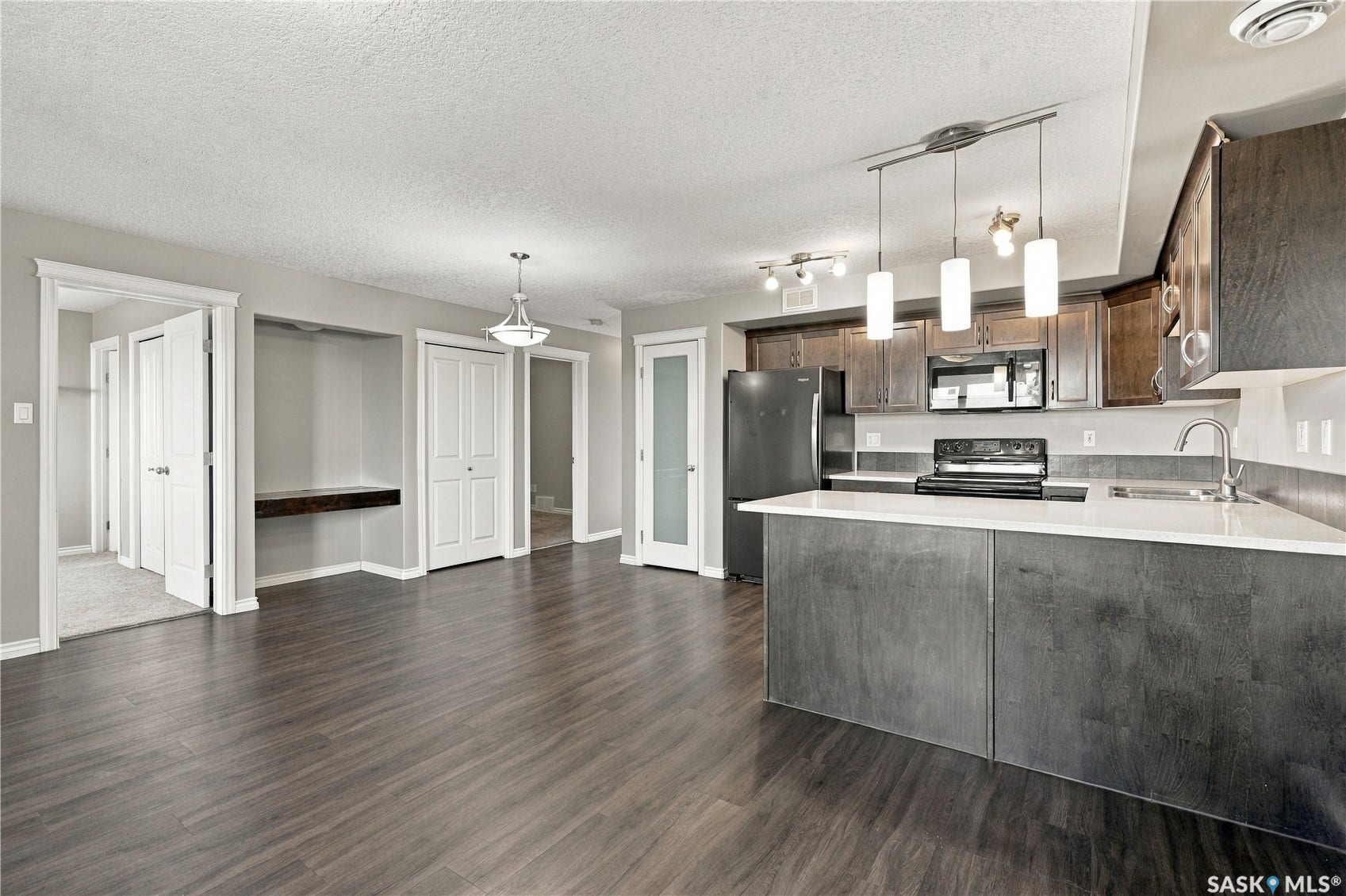 Laminate flooring throughout, kitchen with dark cabinetry, white quartz countertops, built-in microwave, and a breakfast bar island. Primary bedroom is off the living room