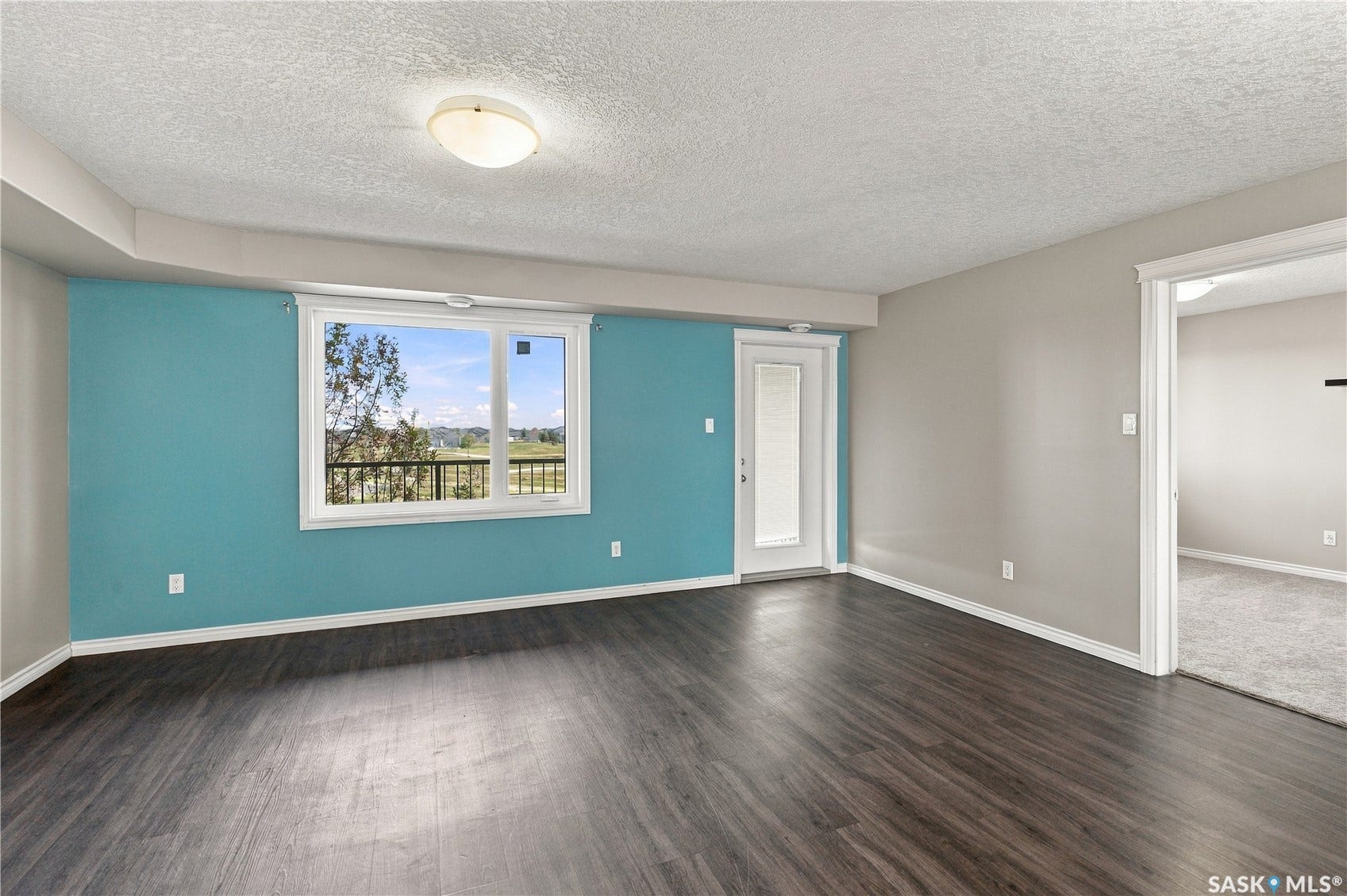 Laminate flooring, a white trim window with views of the park, and a white trim door with inset blinds to the balcony