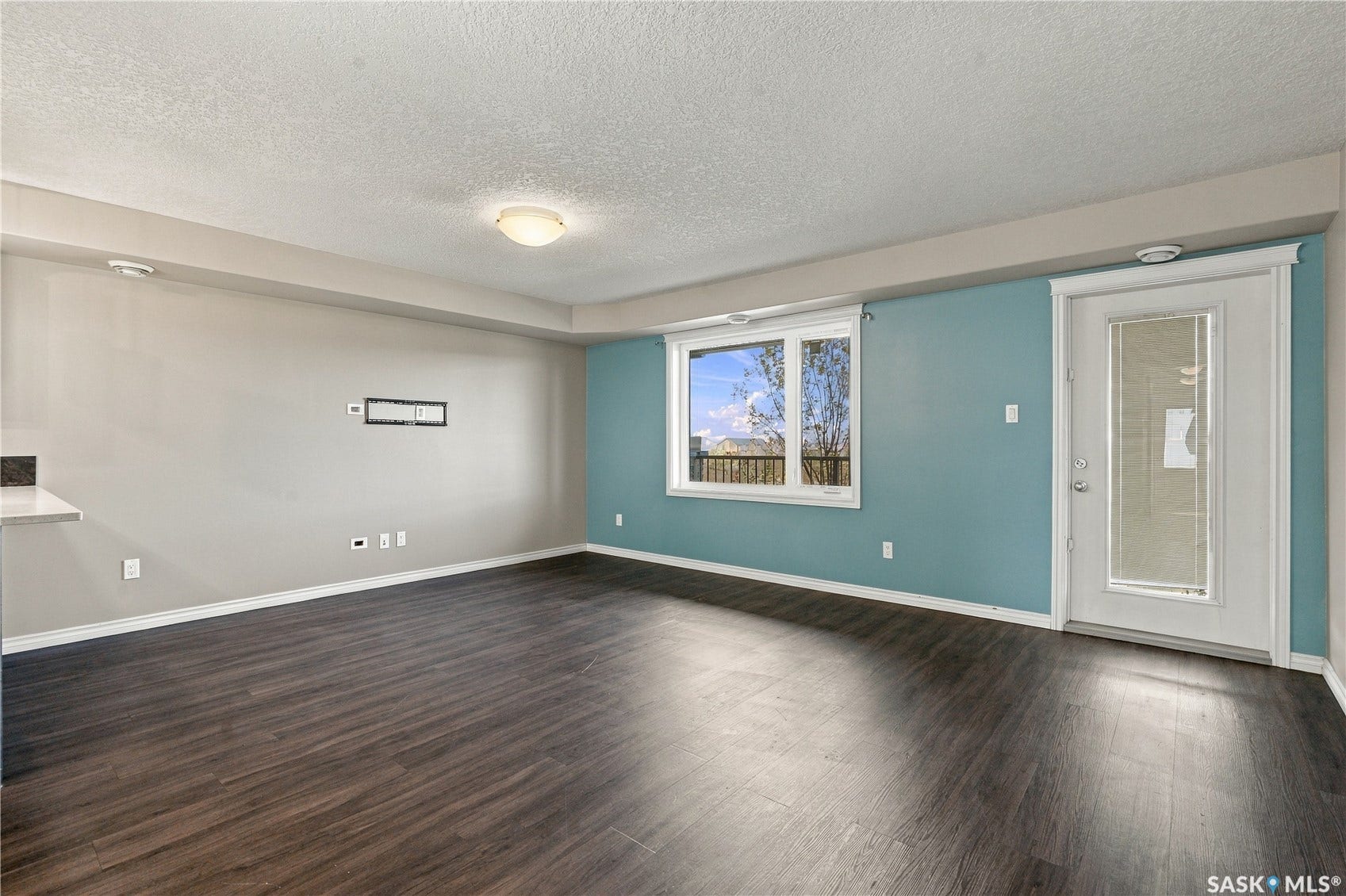 Laminate flooring, a white trim window with views of the park, and a white trim door with inset blinds to the balcony