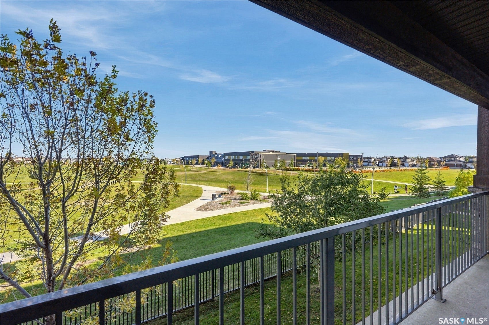 Metal railing overlooking a green space with paved walkways and distant buildings