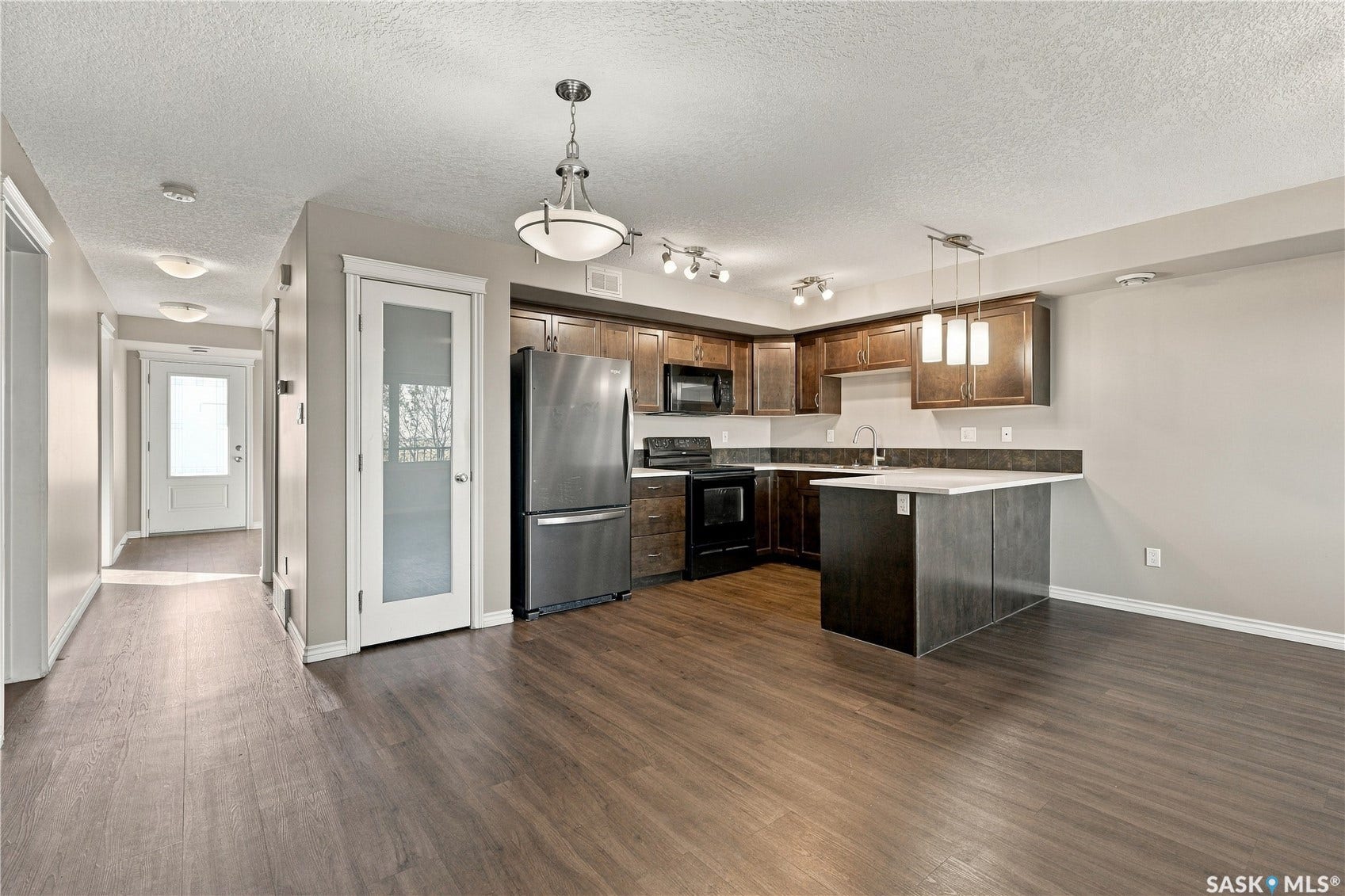 Laminate flooring throughout, kitchen with dark wood cabinetry, appliances and pendant lighting