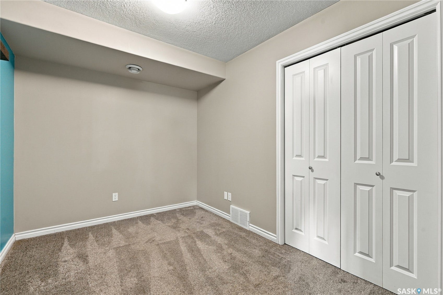 Large den for storage or office space with neutral wall color, carpet flooring, bi-fold closet doors with paneling, white trim, and ceiling light fixture