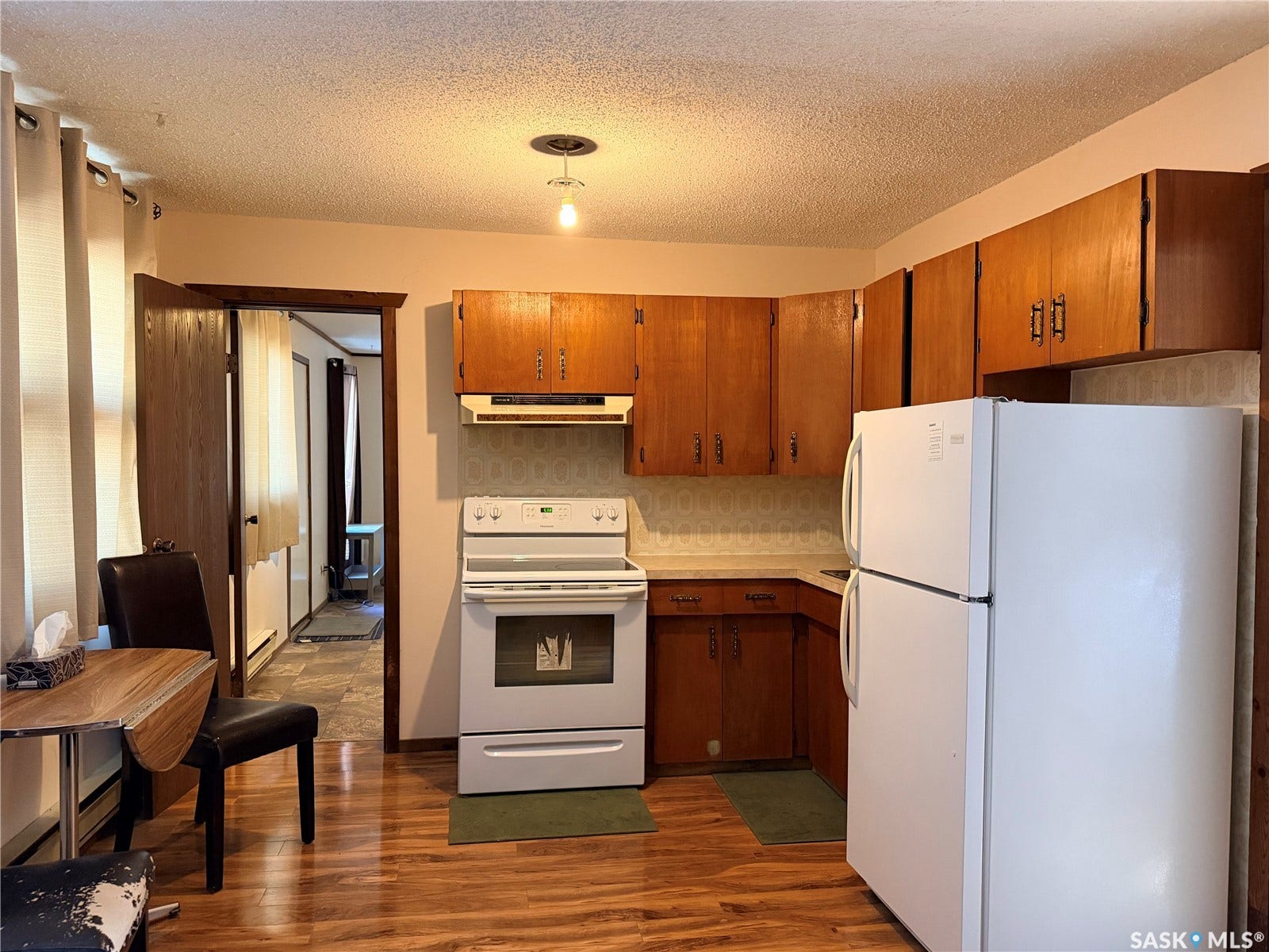 Kitchen featuring wood-finish flooring, wood cabinetry, white appliances, and a built-in range hood
