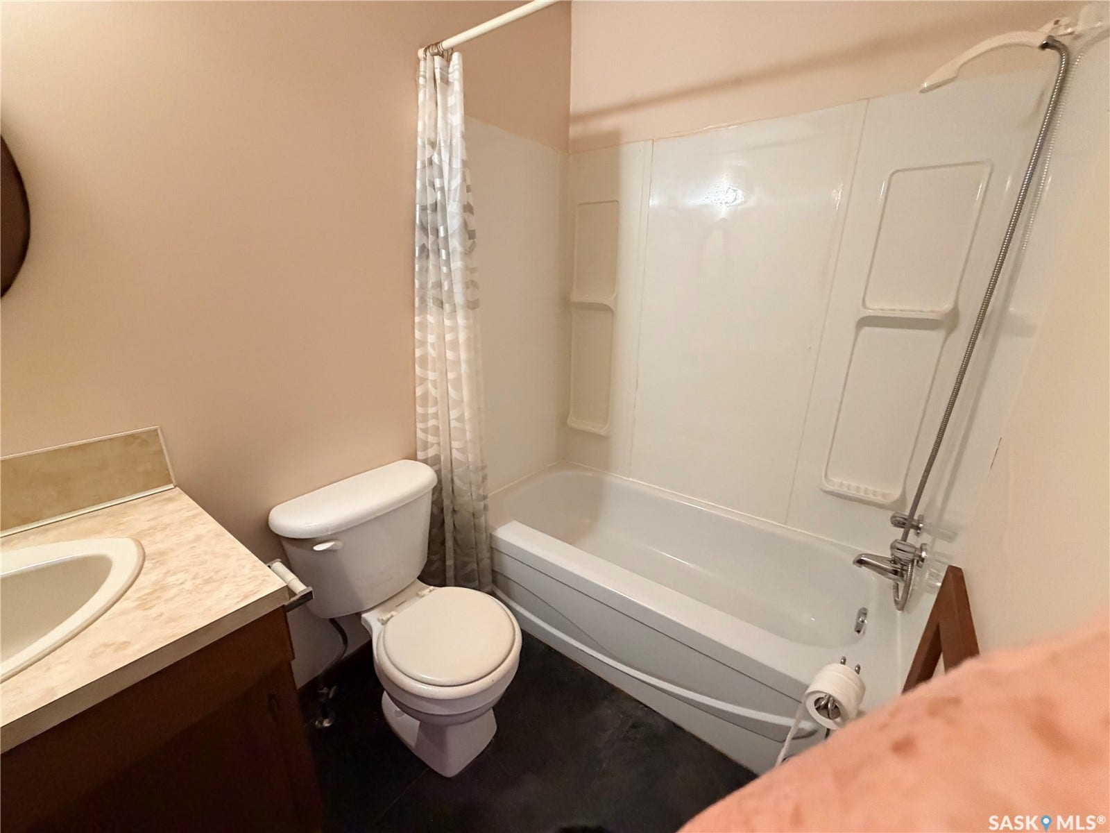 White bathtub with integrated shelving, dark flooring, and a vanity with an integrated sink