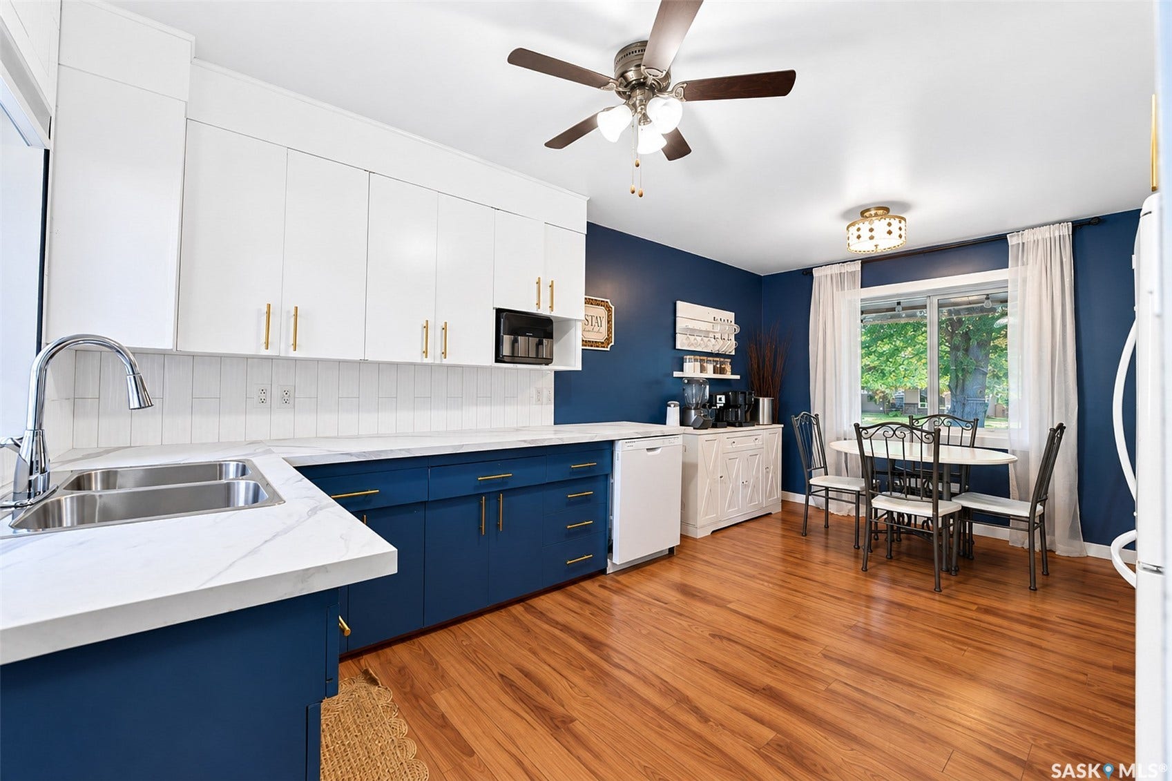 Kitchen featuring two-tone cabinetry with gold-finish hardware, a double basin stainless steel sink, white subway tile backsplash, and wood-finish flooring