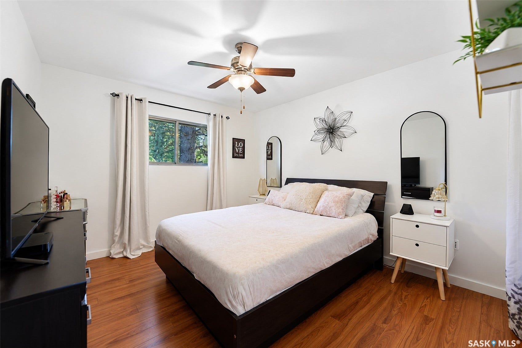 Wood-finish flooring throughout, ceiling fan with integrated lighting, and a window with a dark frame