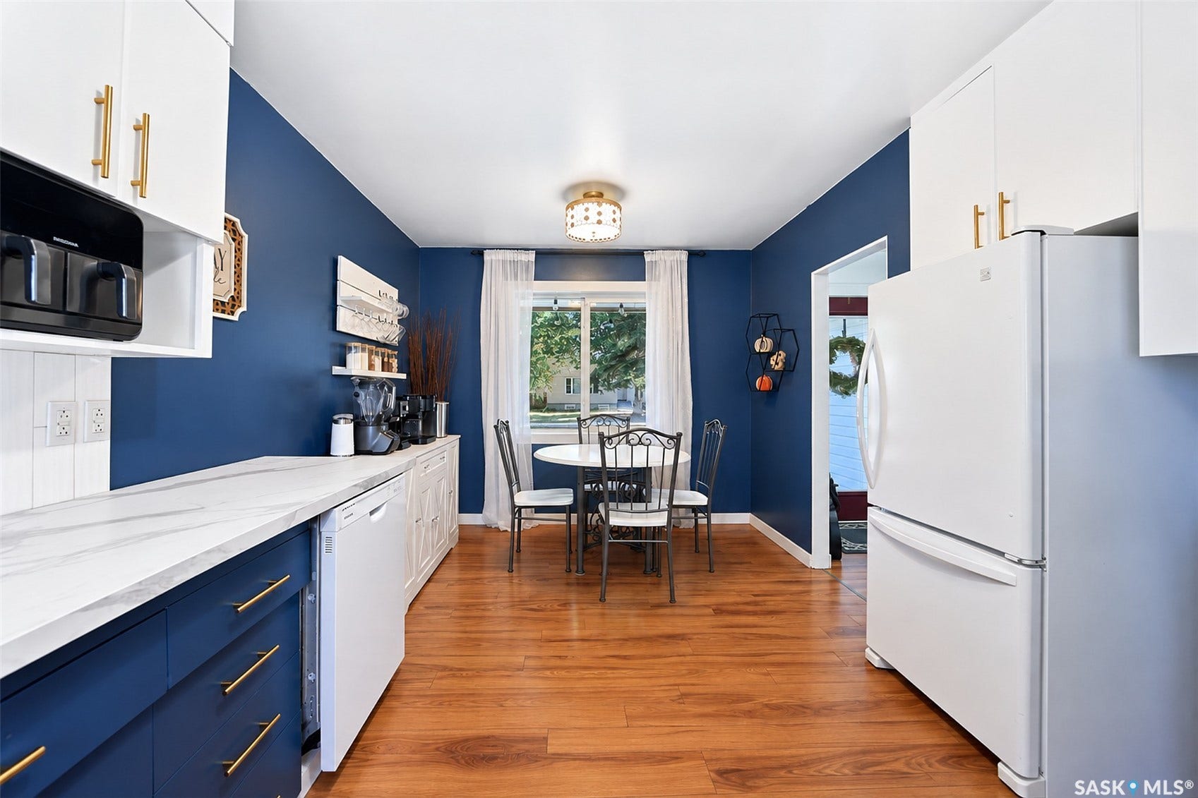 Kitchen with wood-finish flooring, white upper cabinetry, blue lower cabinetry with gold-tone hardware, and white countertops