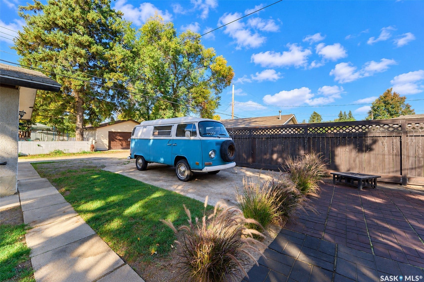 Paved patio area, mature trees, privacy fencing with lattice detail, concrete pathway, and a detached garage structure
