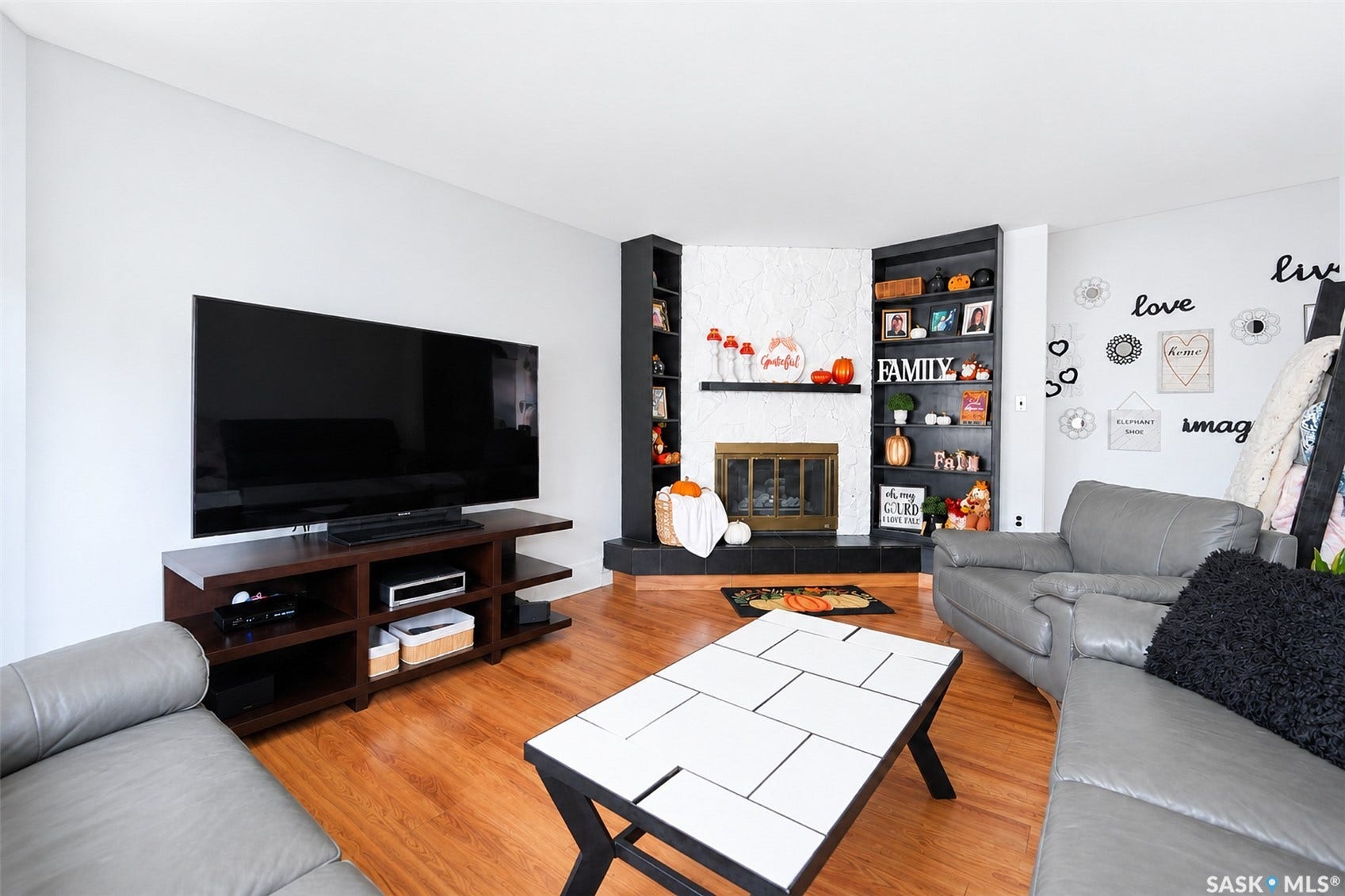 Hardwood-finish flooring, corner fireplace with a brass firebox, white textured mantel, and built-in shelving