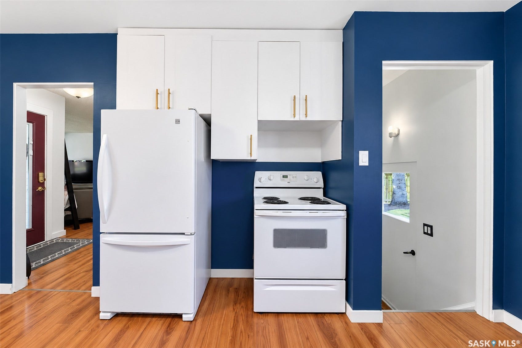 White upper cabinetry with gold-tone pulls, wood-finish flooring, and white appliances