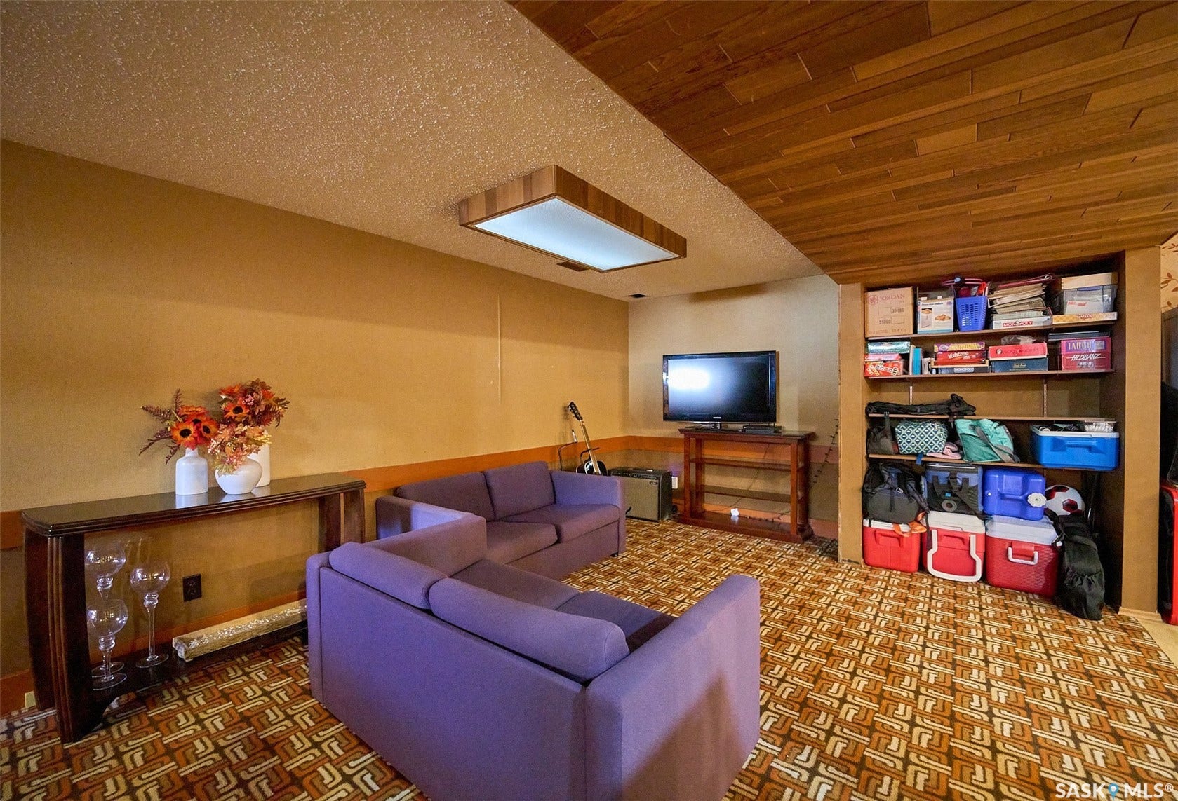 Built-in shelving for storage, wood-paneled ceiling, wall-mounted light fixture, and wood-finish console table