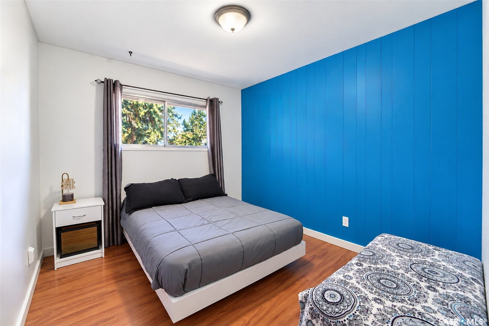 Wood-finish flooring with a blue accent wall and white walls, featuring a window with exterior tree scenery