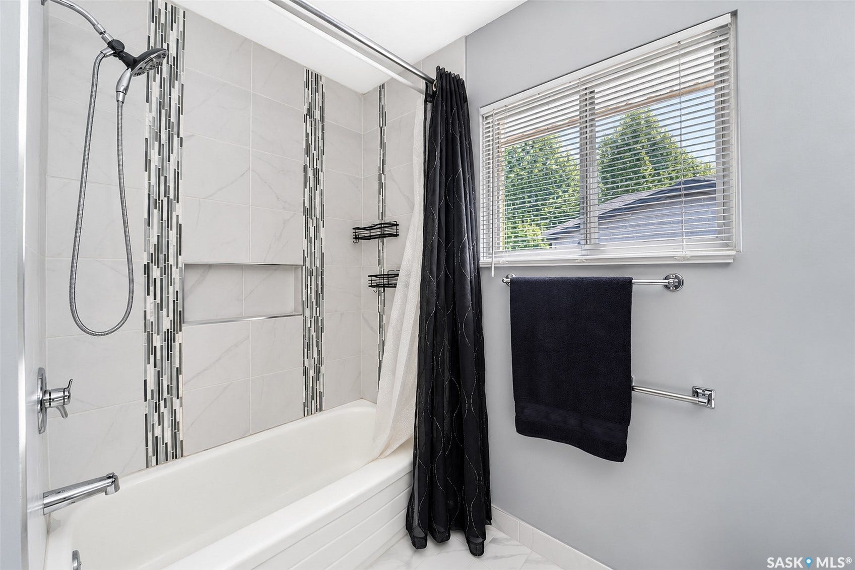 Bathtub with a tiled surround featuring decorative vertical mosaic accents and recessed shelving