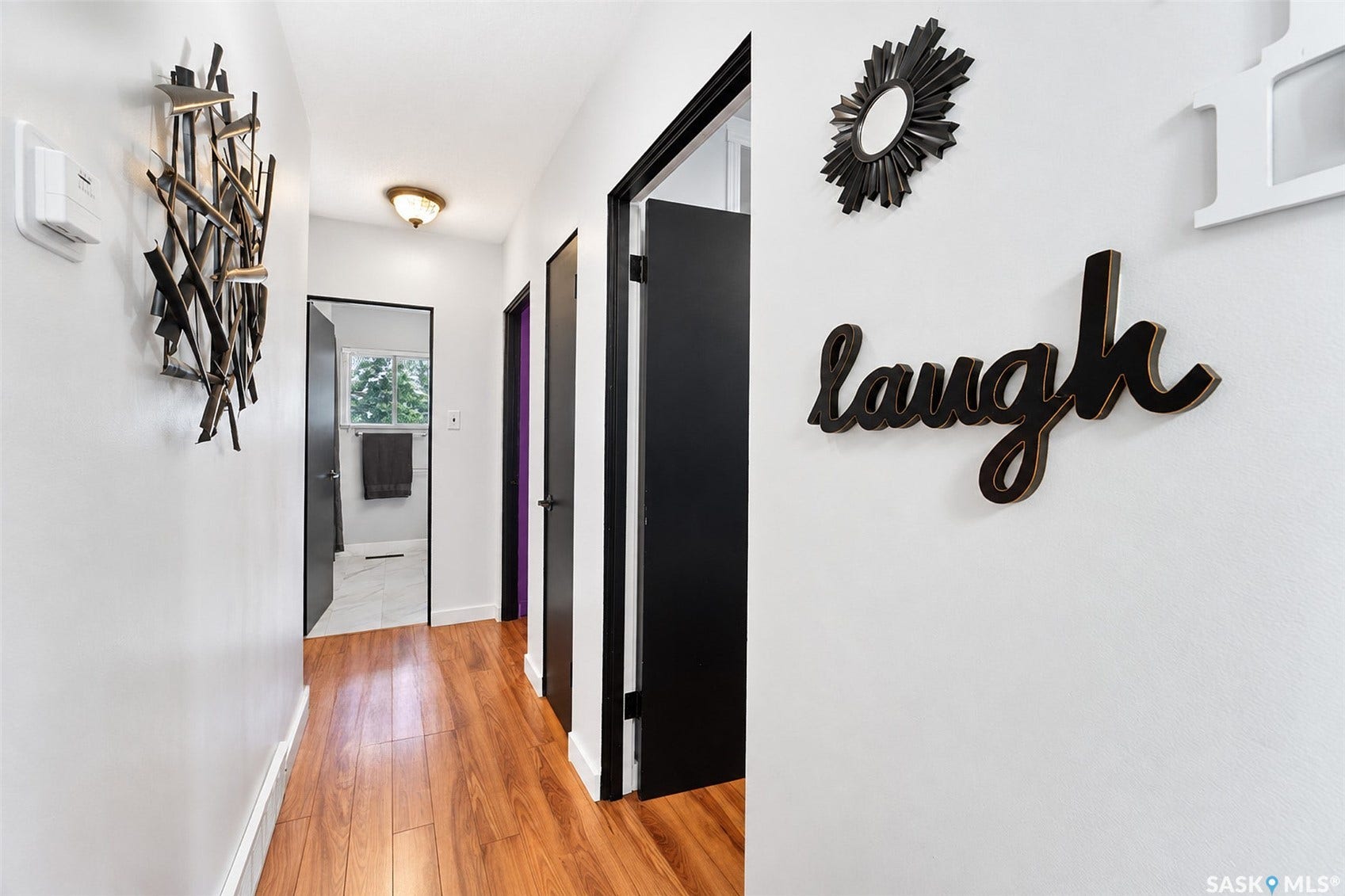 Bright hallway featuring warm wood-finish flooring, white walls, and black-framed interior doors with contrasting trim