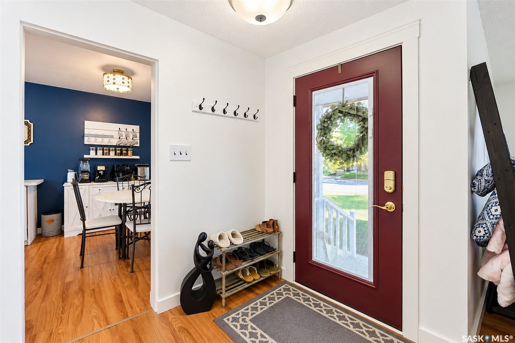 Welcoming foyer with rich hardwood flooring, burgundy entry door with glass panel and brass hardware, coat hooks, and shoe storage