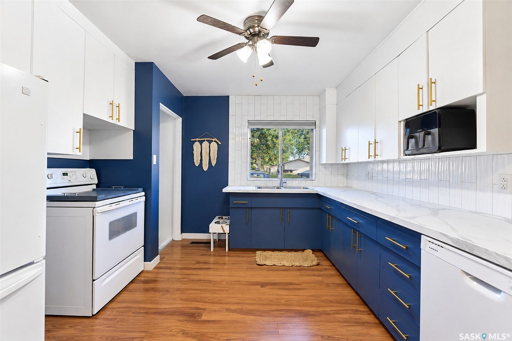 Kitchen featuring wood-finish flooring, white appliances, white upper cabinetry with gold-tone hardware, blue lower cabinetry with gold-tone hardware, and a white tile backsplash