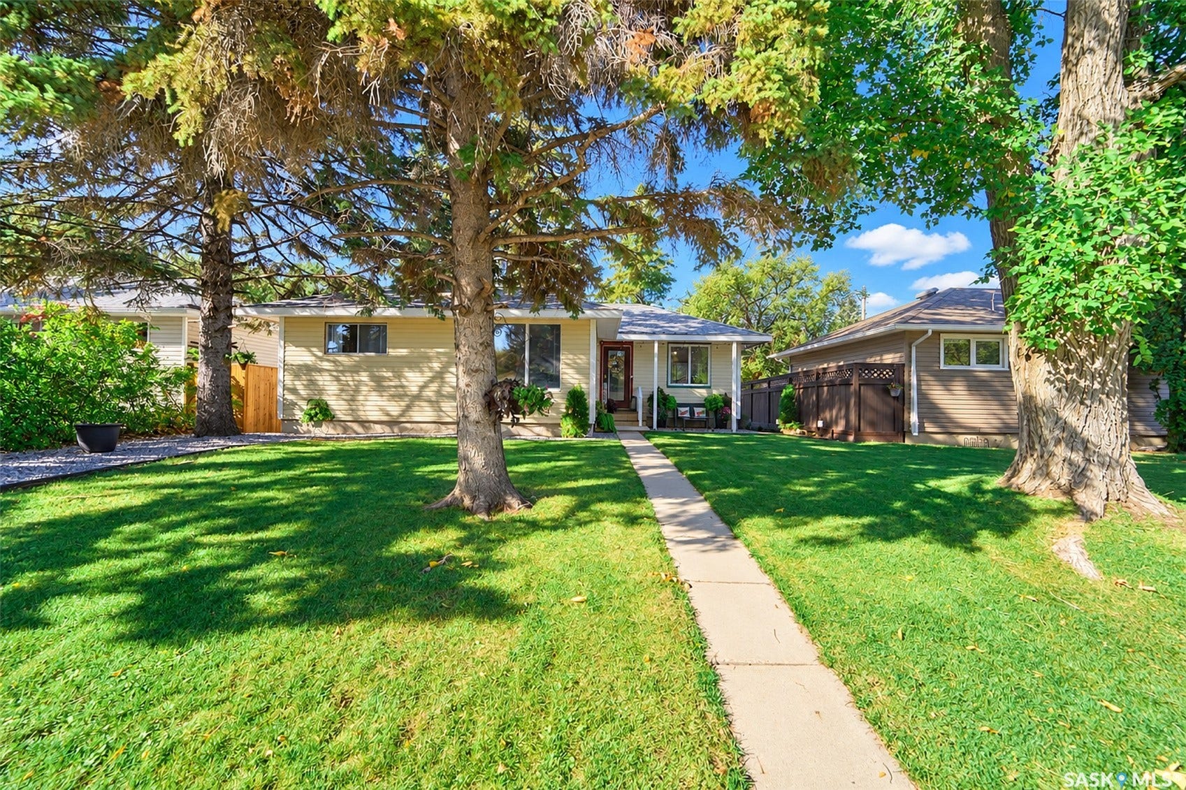 Manicured front lawn with mature trees, concrete walkway, and a covered front porch