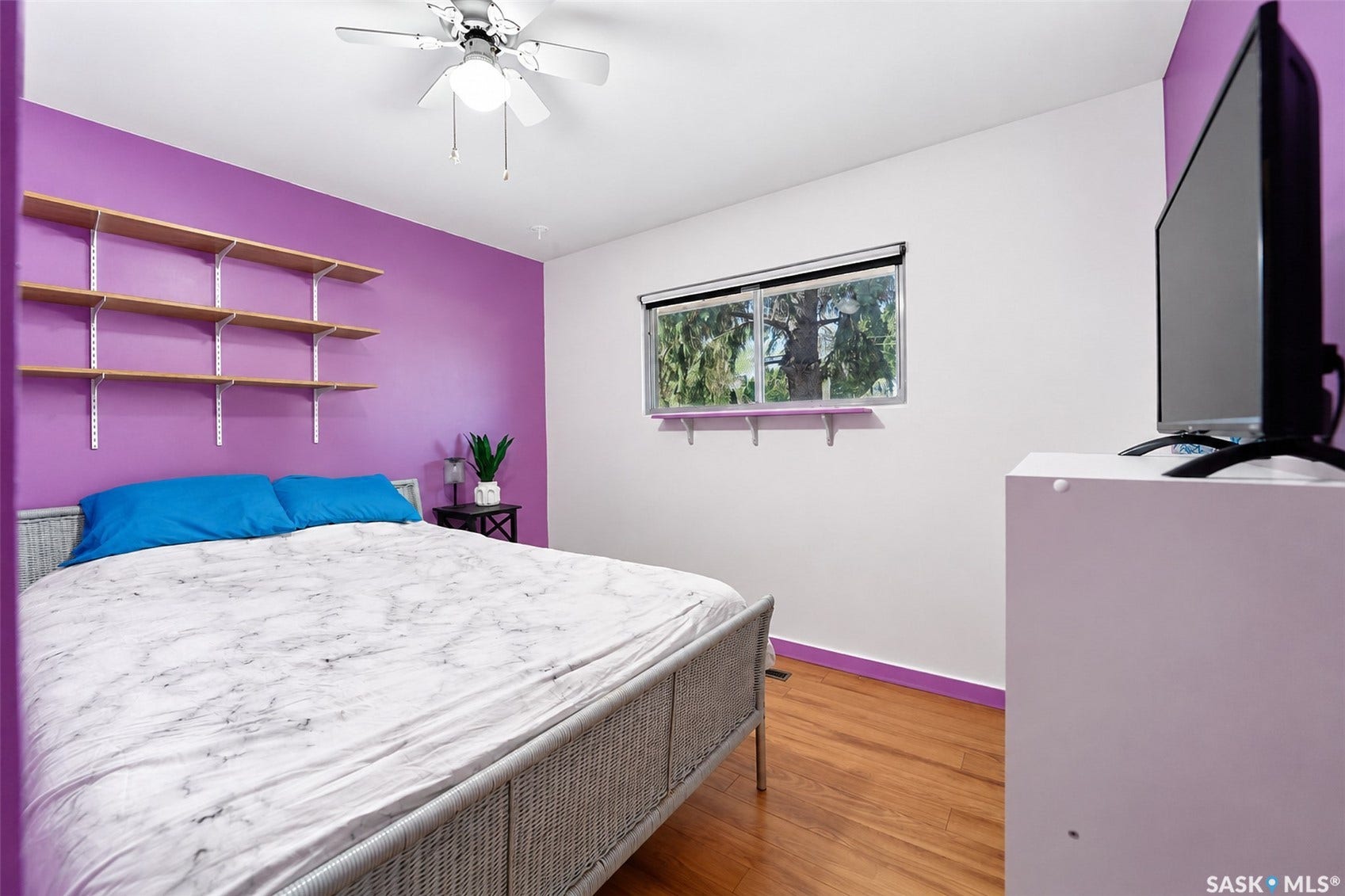 Wood-finish flooring, ceiling fan with integrated lighting, built-in shelving, and a window with roller shade