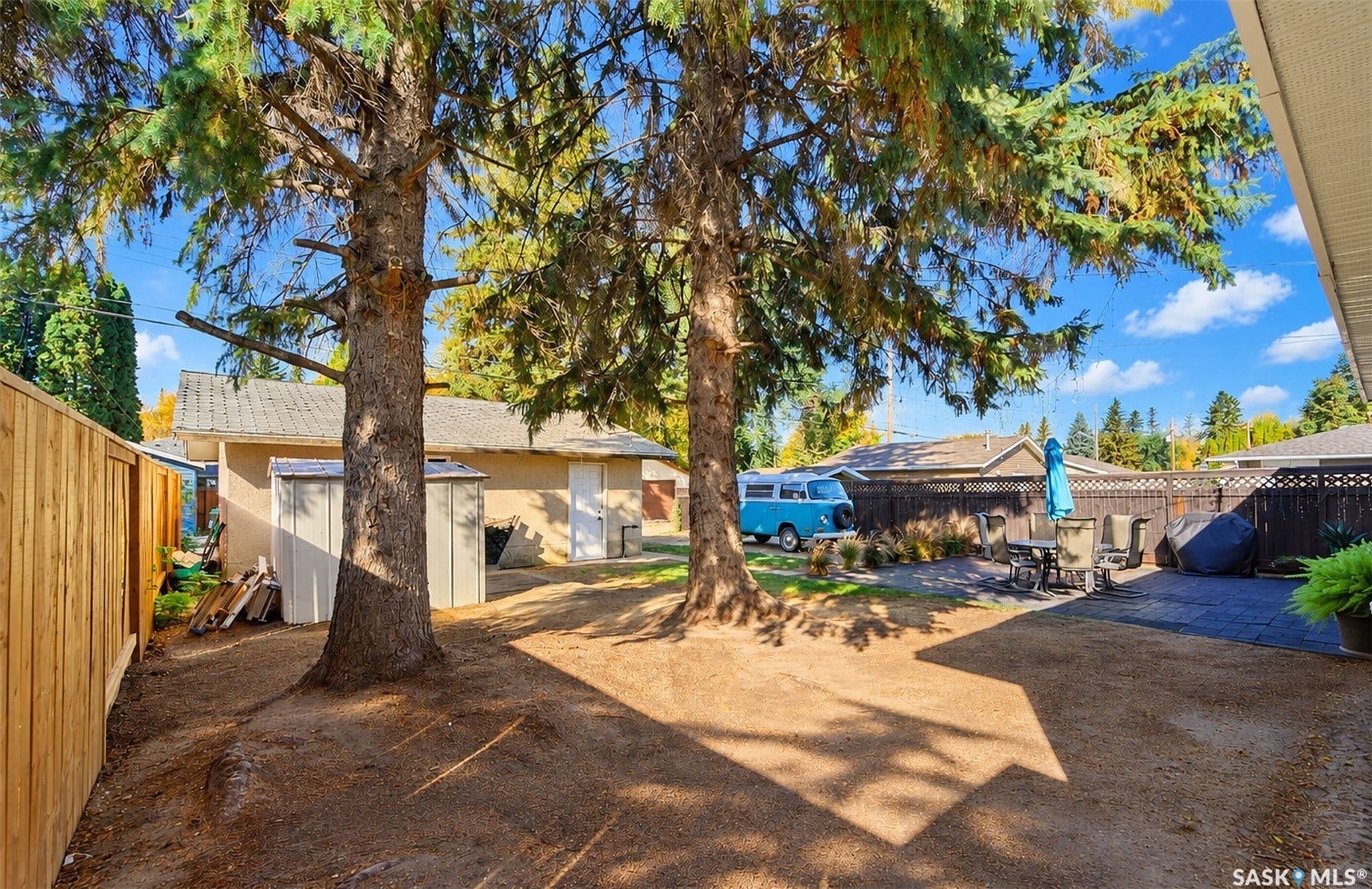 Expansive outdoor area featuring mature trees, a wooden fence, and a paved patio area