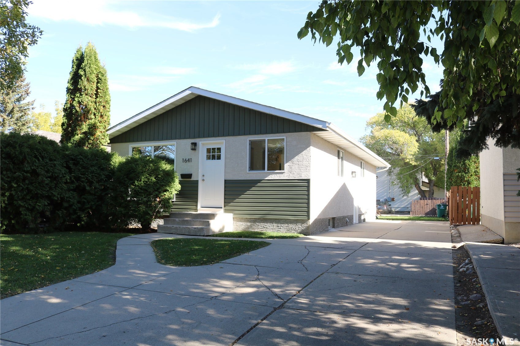 1641 Thompson Avenue, Saskatoon SK S7N 1Y2 Bungalow featuring stucco and horizontal panel siding, a concrete driveway, established landscaping, and a concrete front pathway