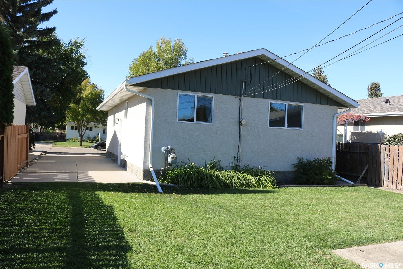 1641 Thompson Avenue, Saskatoon SK S7N 1Y2 Expansive rear yard featuring a manicured lawn, concrete driveway, and stucco exterior with white trim