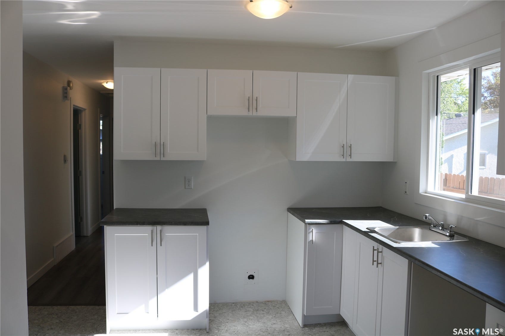1641 Thompson Avenue, Saskatoon SK S7N 1Y2 White shaker-style cabinetry, dark countertops, stainless steel sink with faucet, white window trim, and overhead lighting