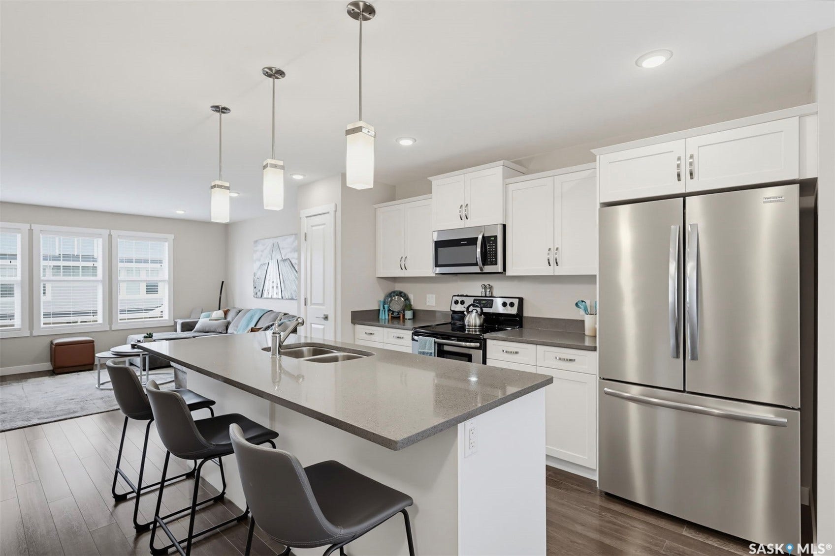 Open-concept kitchen with white shaker cabinetry, stainless steel appliances, a center island with double sink, and pendant lighting