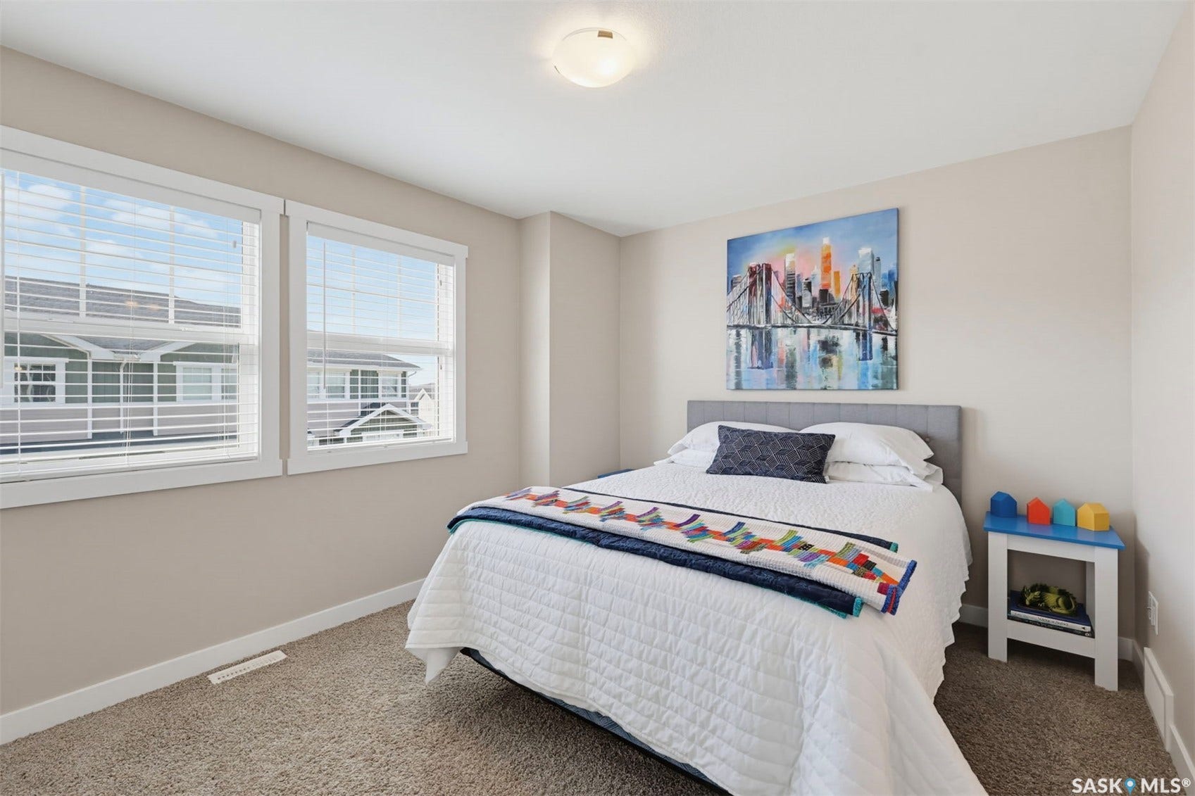 Neutral-toned walls, plush carpet flooring, two white-framed windows with blinds, and a flush mount ceiling light