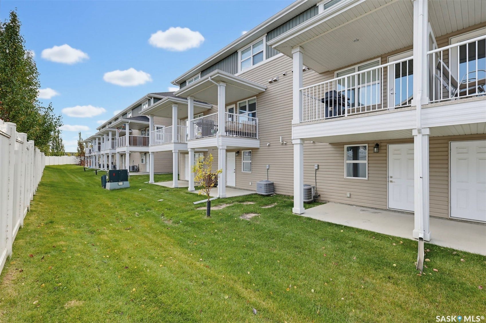 Expansive green space featuring a white privacy fence, individual ground-level patios, and upper-level balconies with white railings
