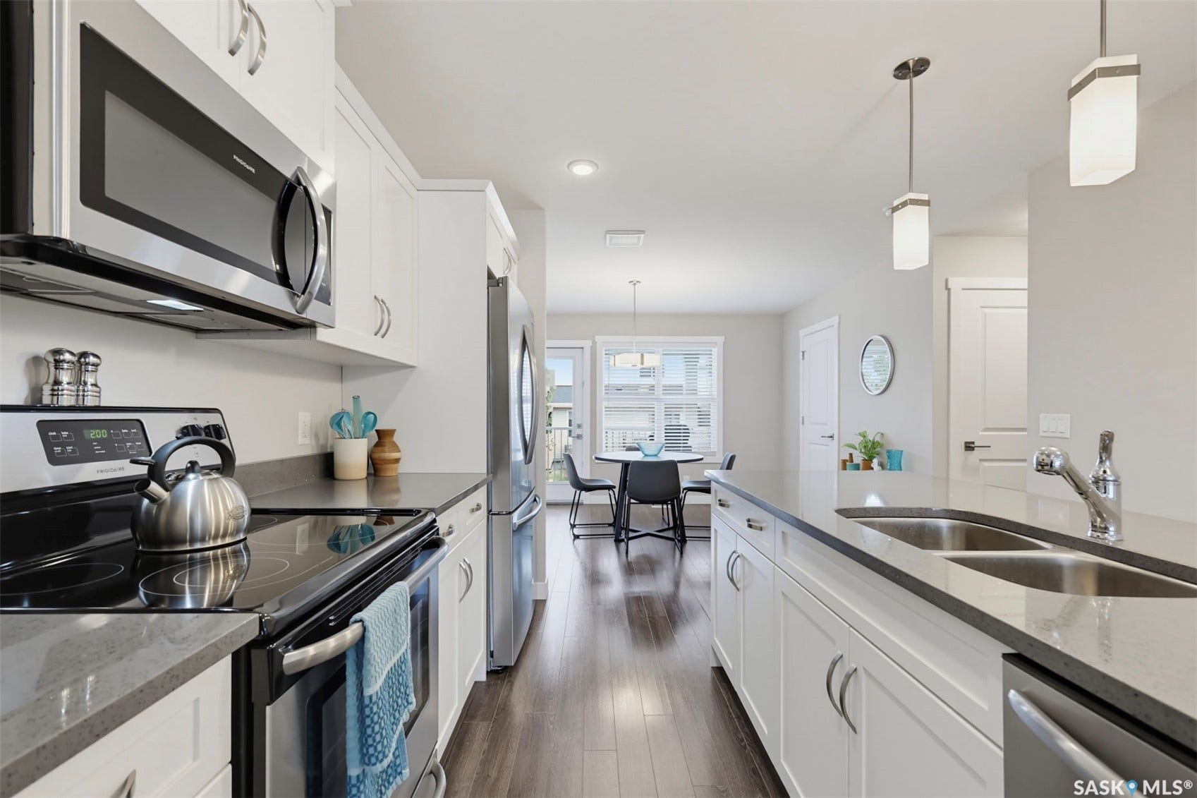 Modern kitchen featuring stainless steel appliances, white cabinetry, dark countertops, a double basin sink, and wood-finish flooring