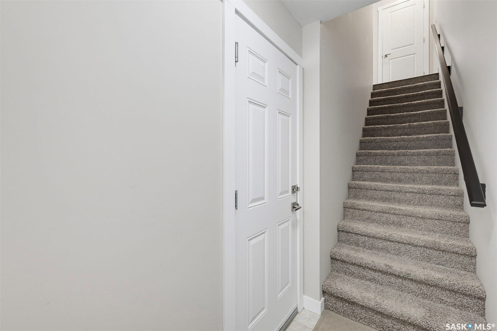 Carpeted staircase with dark handrail and white paneled door