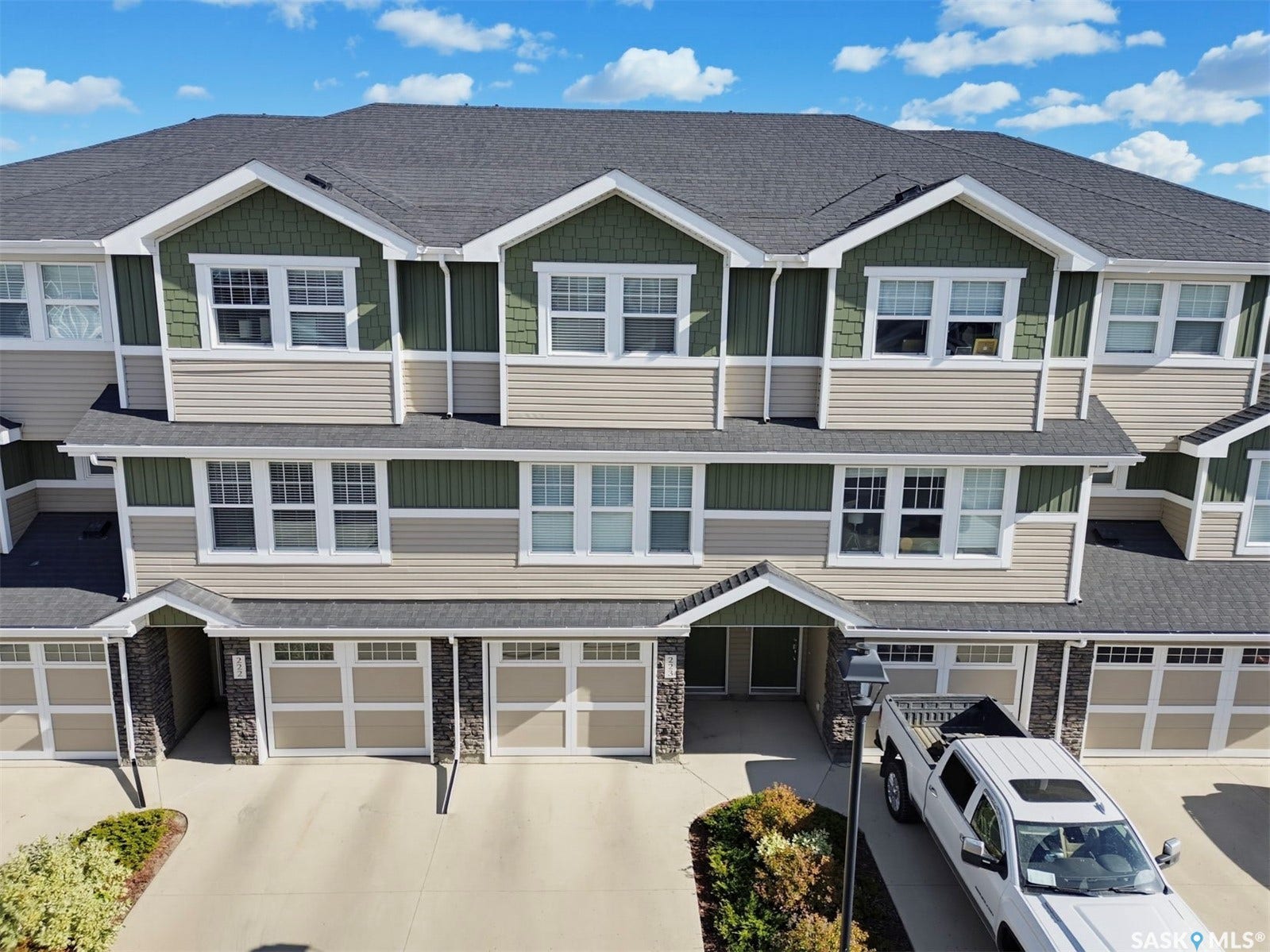 Multi-level townhome exterior featuring an asphalt shingle roof, green and tan siding, and white window frames