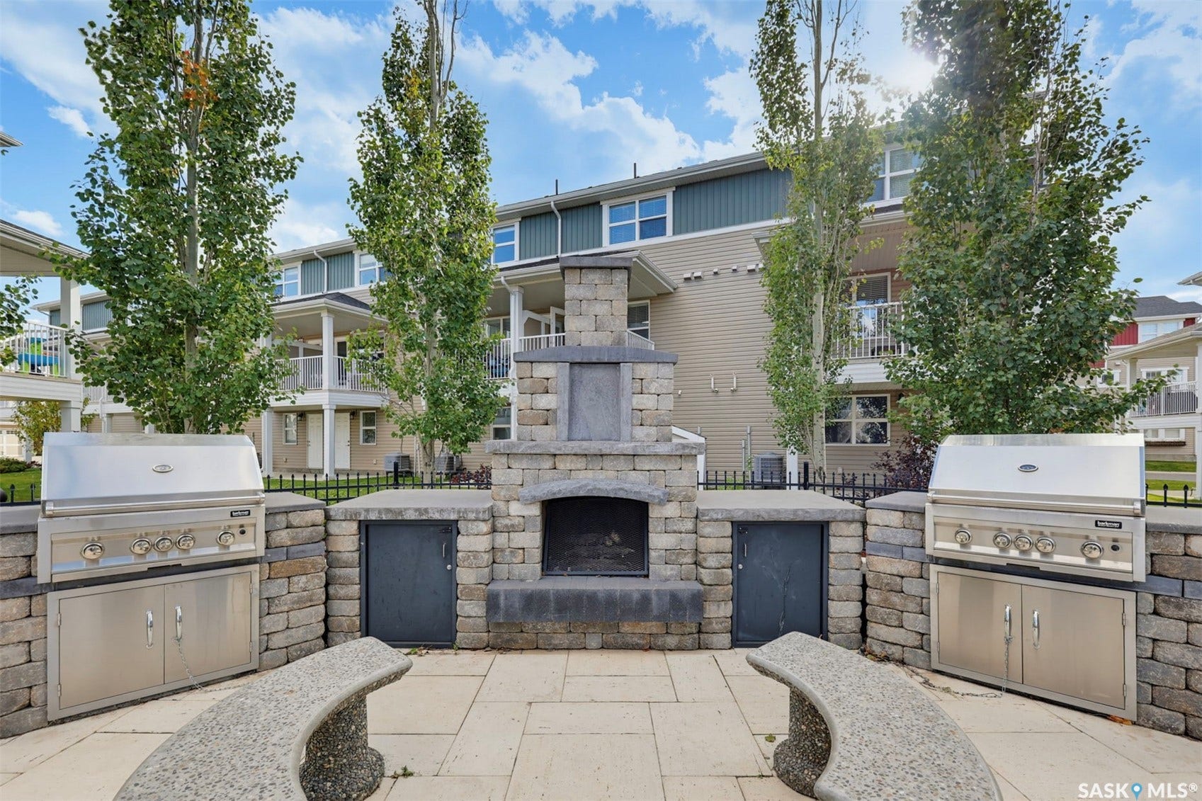 Outdoor living area featuring two stainless steel grills, a stone-clad fireplace, and paver patio