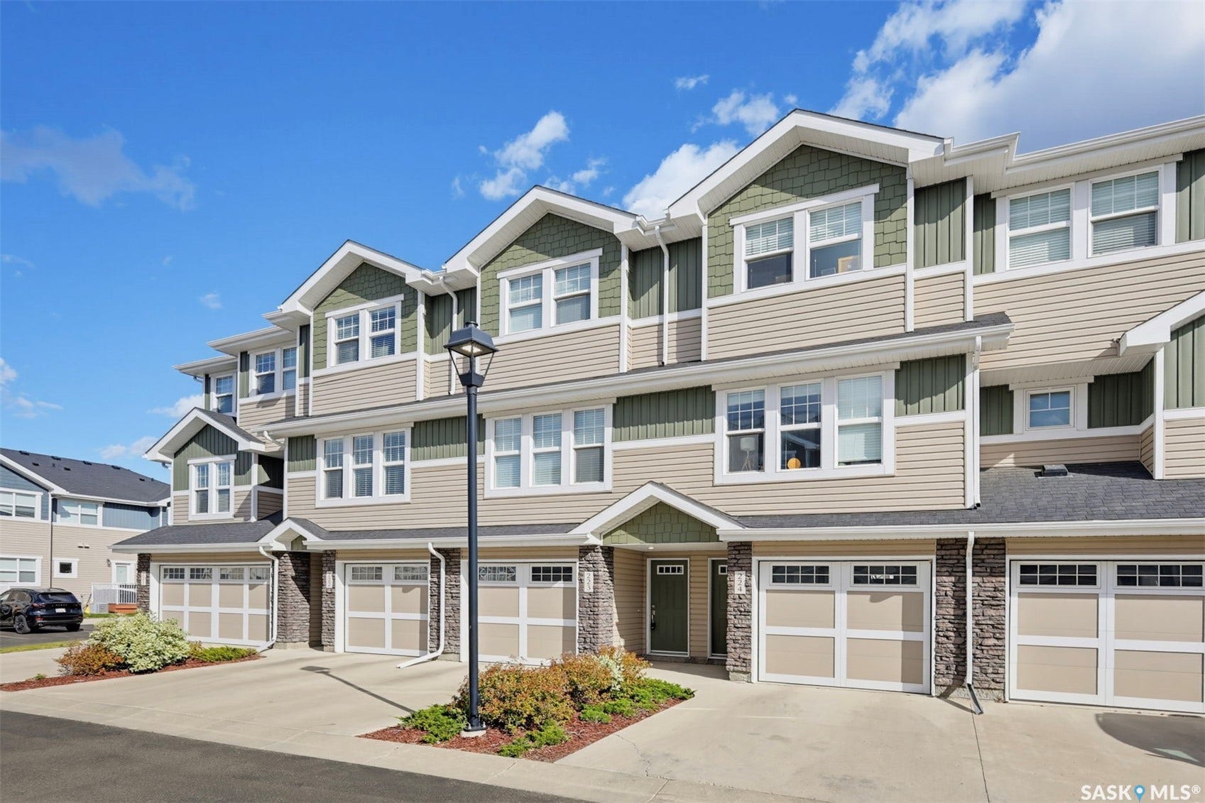 Multi-level townhome featuring a stone and siding exterior, multiple windows, and an attached garage with a paved driveway