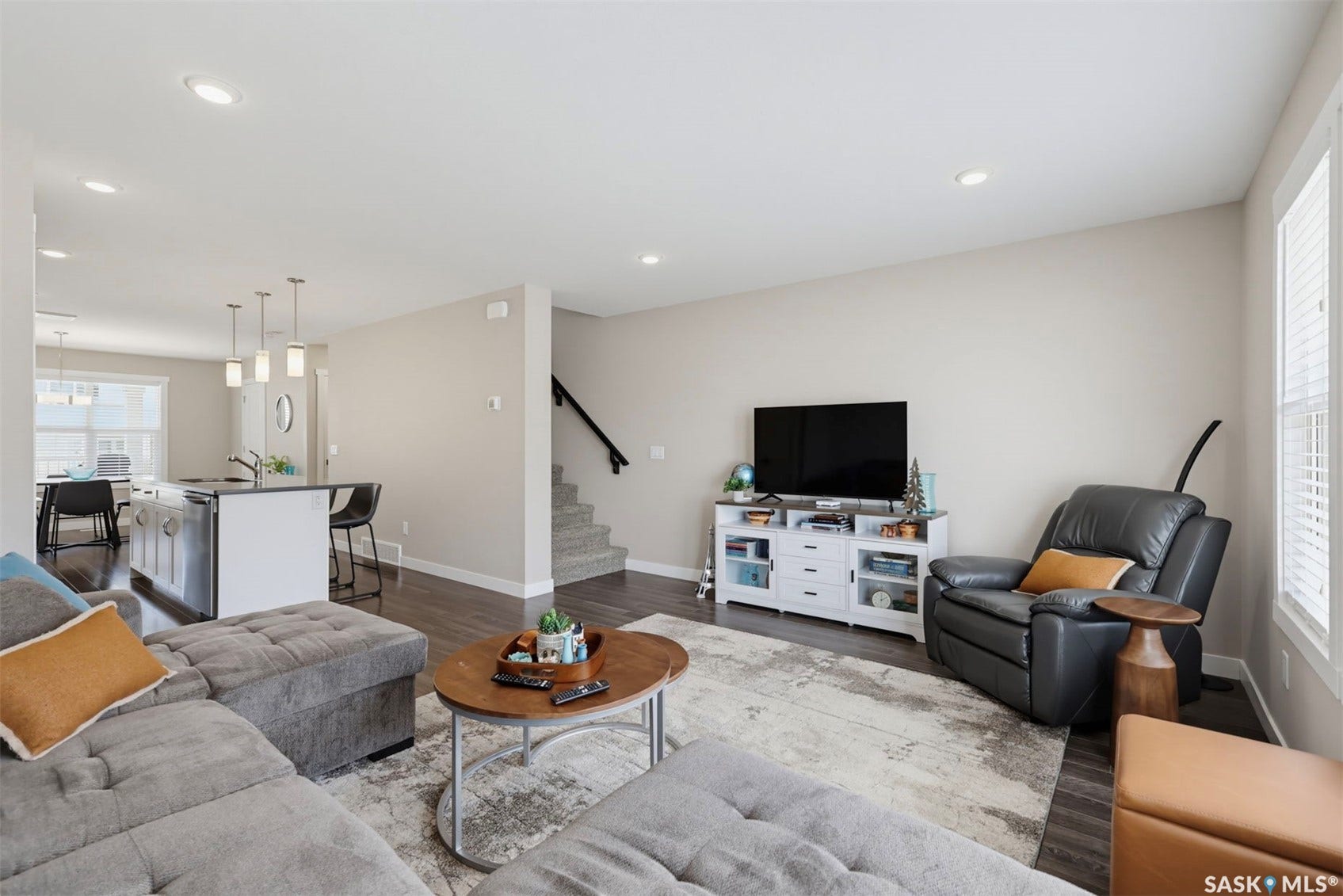 Open-concept living area featuring recessed lighting, wood-finish flooring, a kitchen island with pendant lighting, and a staircase with a dark handrail