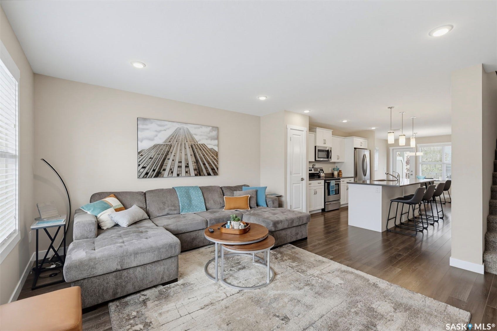 Open-concept living area featuring recessed lighting, wood-finish flooring, and a kitchen with white cabinetry, stainless steel appliances, and a central island with pendant lighting