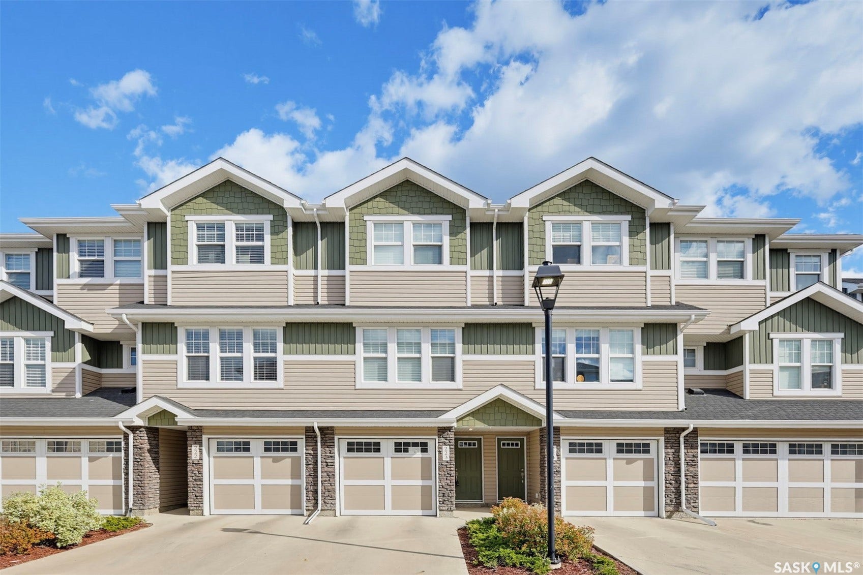 Multi-level townhome exterior featuring an attached garage, dormer windows, and a combination of horizontal siding and shingle accents