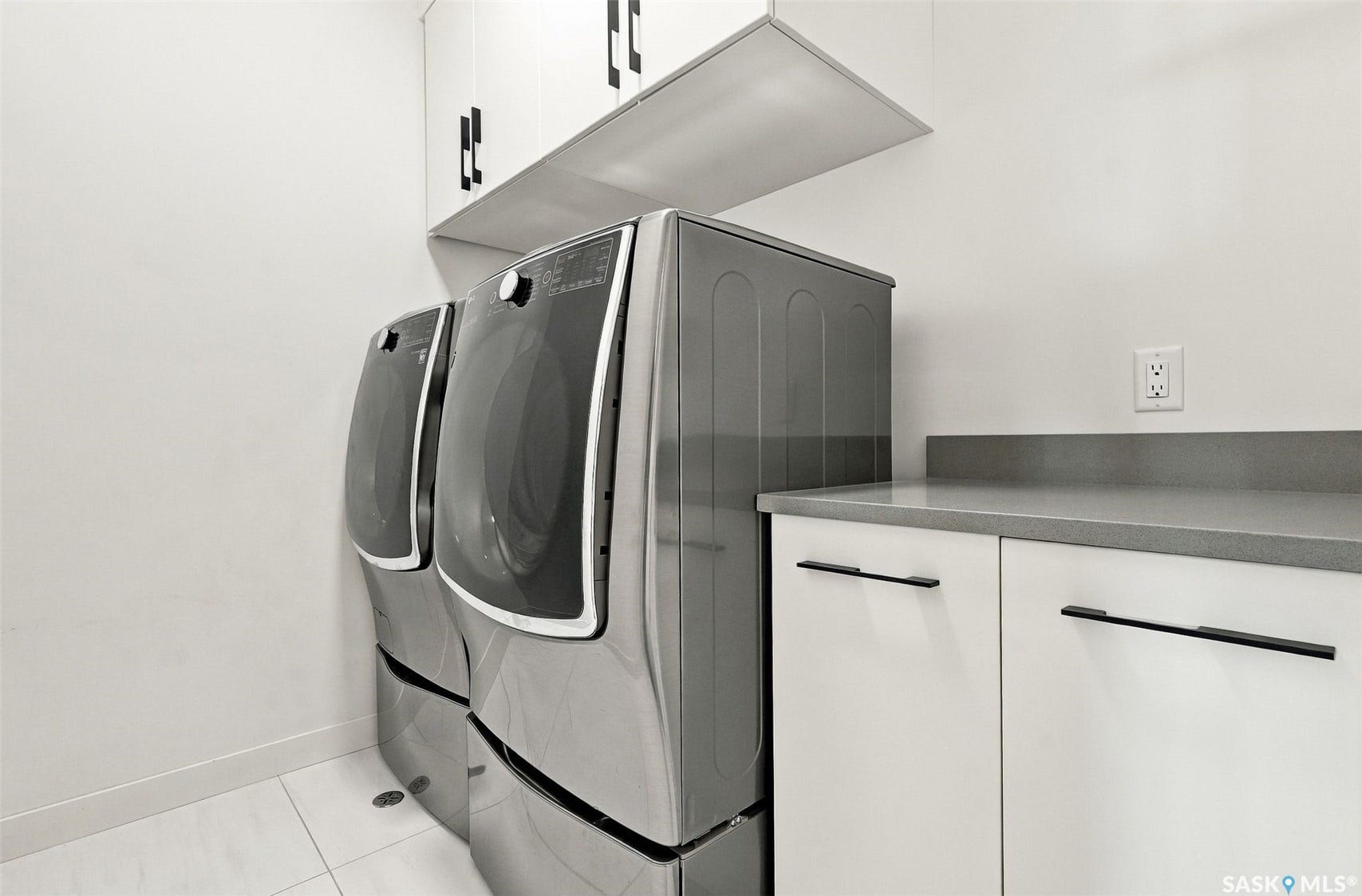 6221 Koep Avenue, Regina SK S4X 0J2 Dedicated laundry area featuring a washer and dryer, white cabinetry with black hardware, a grey countertop, and white floor tiles