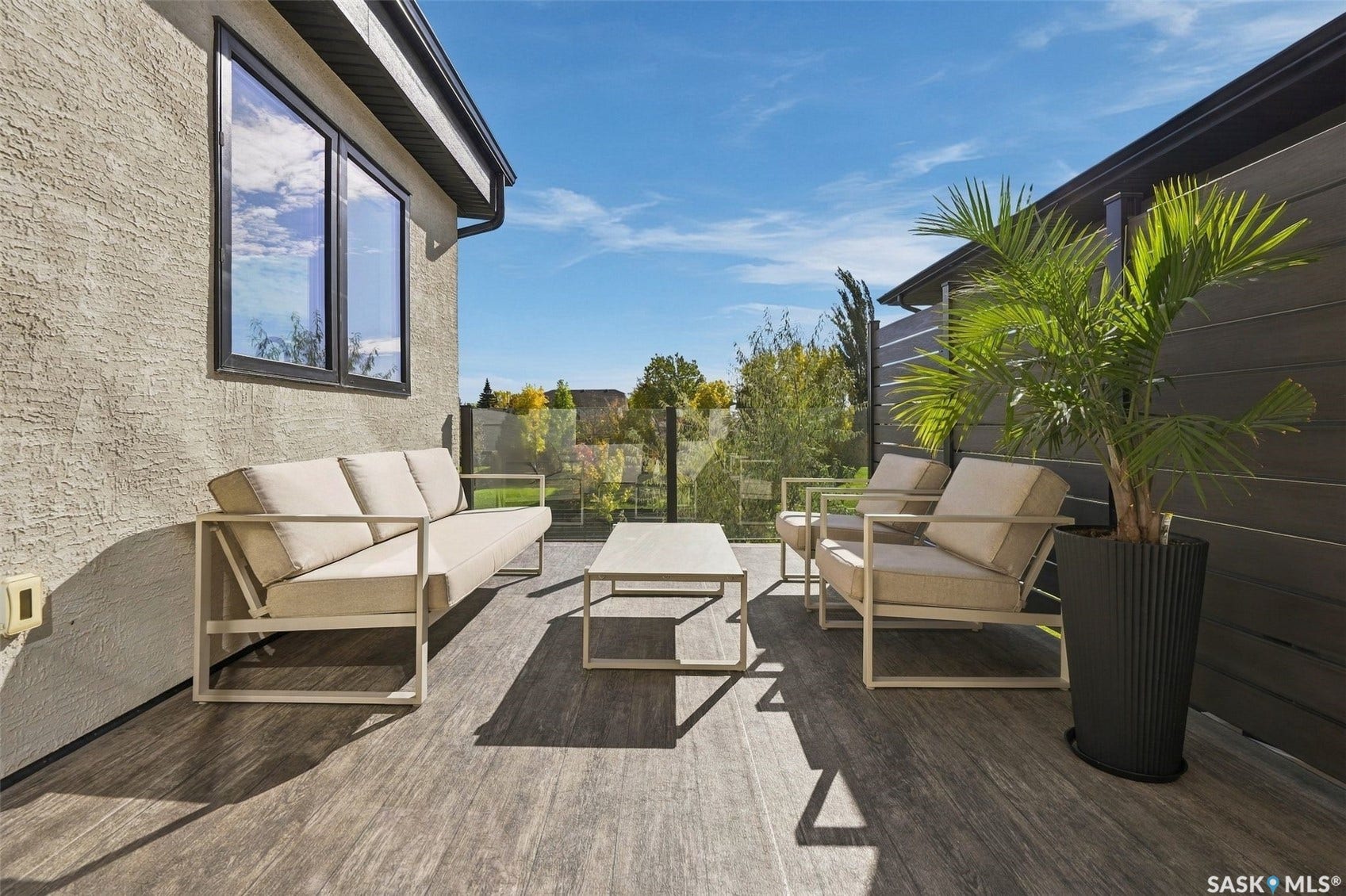 6221 Koep Avenue, Regina SK S4X 0J2 Outdoor patio featuring wood-finish decking, glass panel railing, textured exterior stucco, and horizontal plank fencing