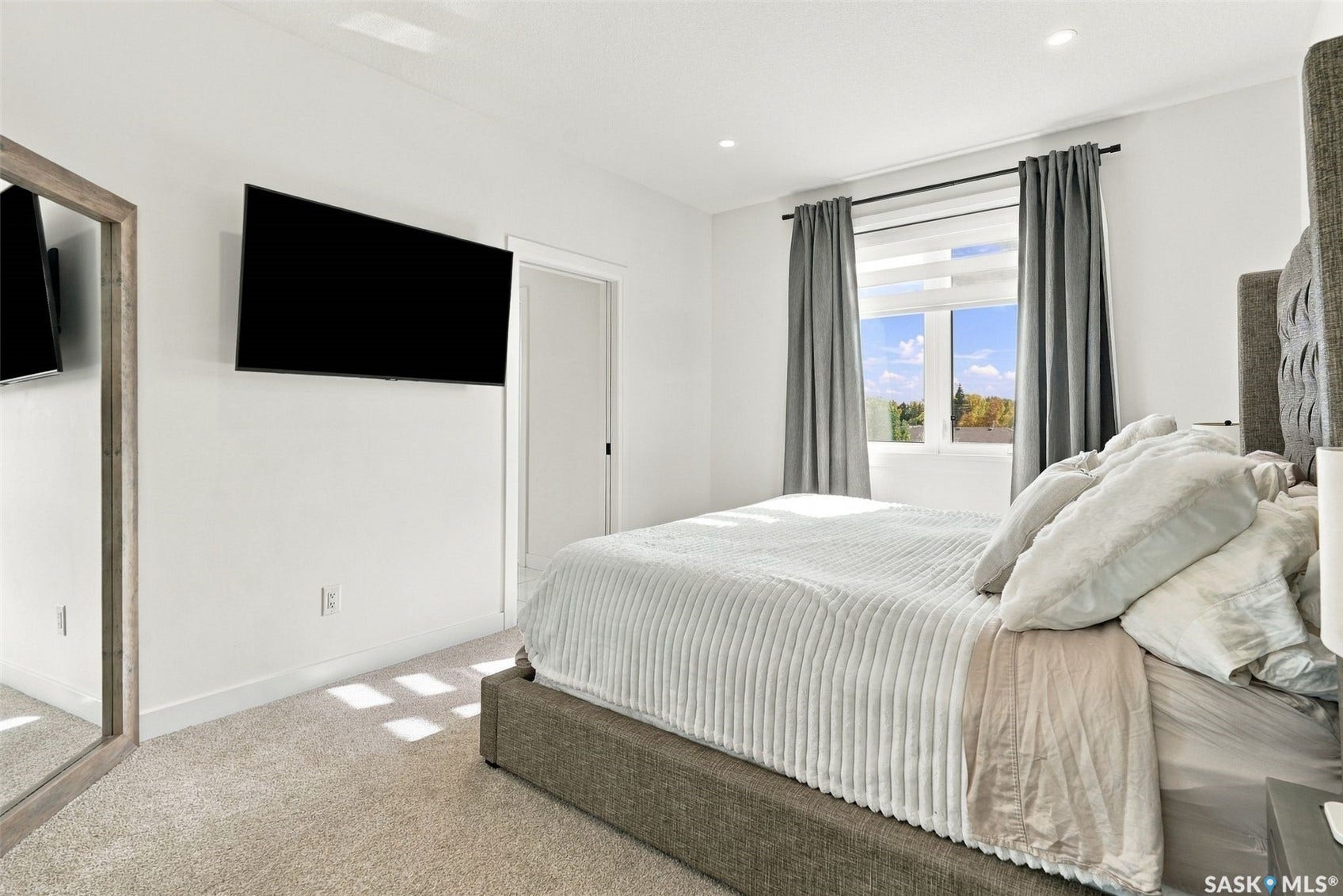 6221 Koep Avenue, Regina SK S4X 0J2 Recessed lighting illuminates neutral carpeting and a white wall, featuring a mounted screen and a window with roller shades and drapery