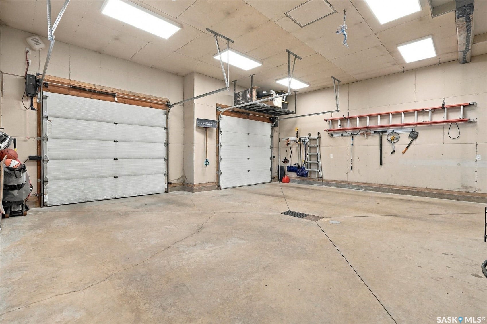 6221 Koep Avenue, Regina SK S4X 0J2 Two overhead garage doors, concrete flooring, overhead fluorescent lighting, wall-mounted storage racks, and overhead storage shelving