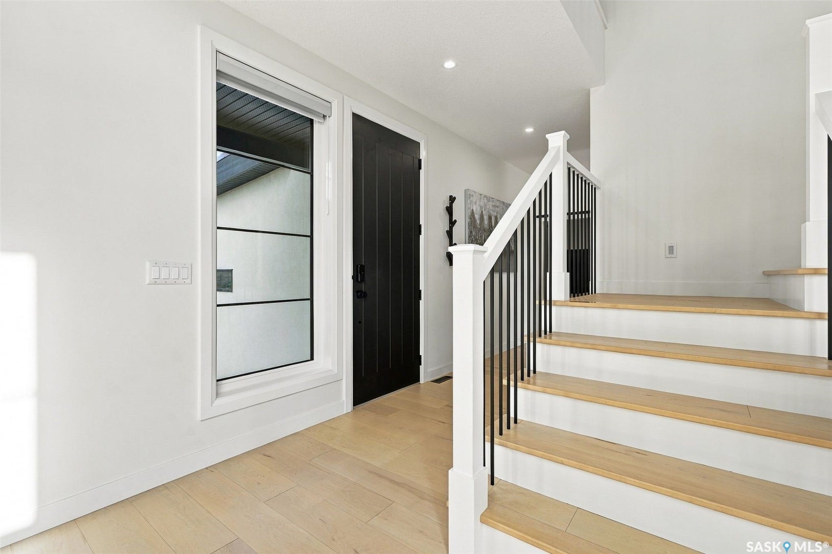 6221 Koep Avenue, Regina SK S4X 0J2 Light wood-finish flooring, staircase with white risers, wood treads, and black iron balusters, black interior door, and a tall window